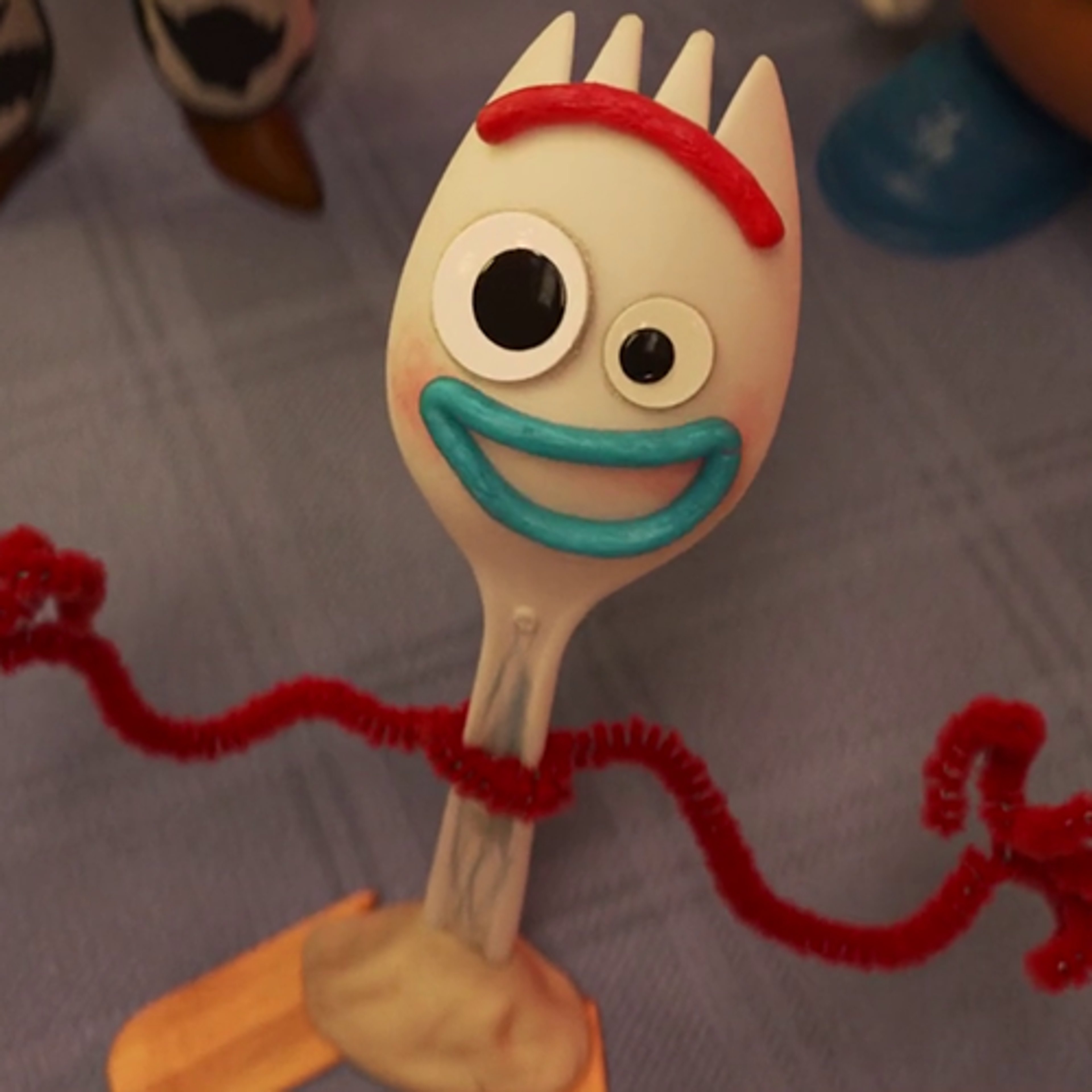 A handcrafted toy character named Forky, made from a plastic spork, googly eyes, wax sticks, pipe cleaners, and popsicle sticks.