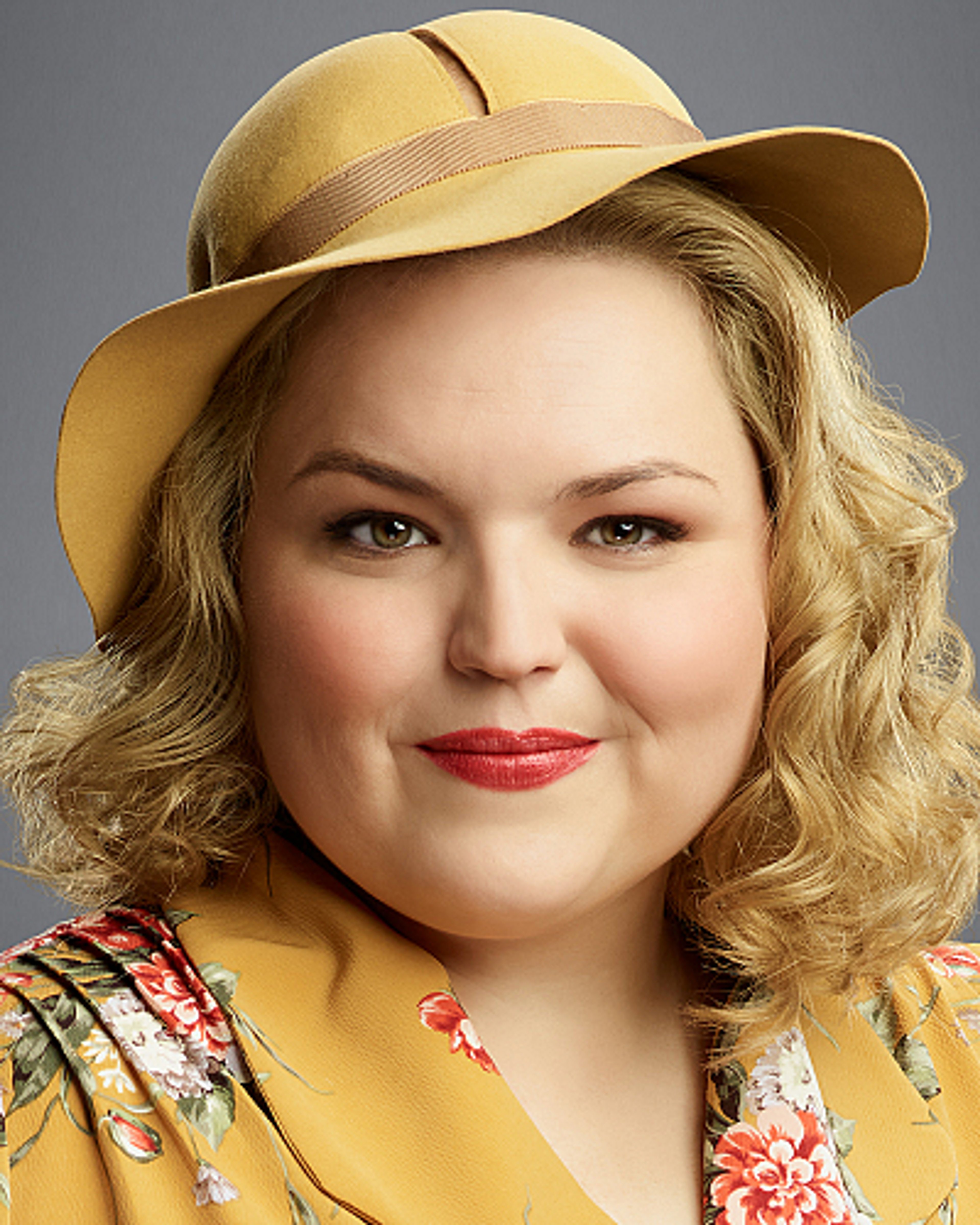 A woman with curly blonde hair wearing a yellow hat and floral dress