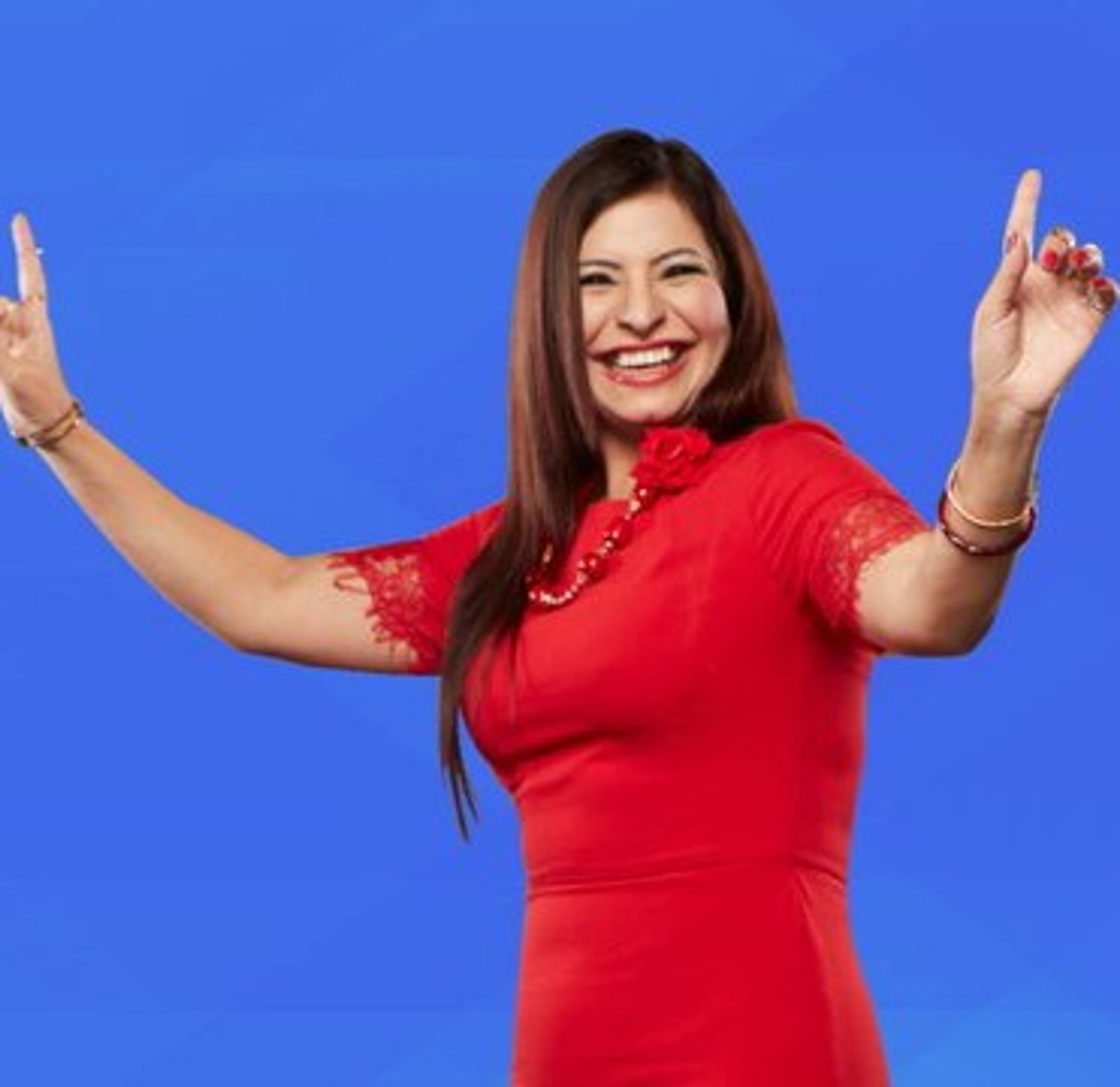 A smiling woman in a red dress with her arms raised