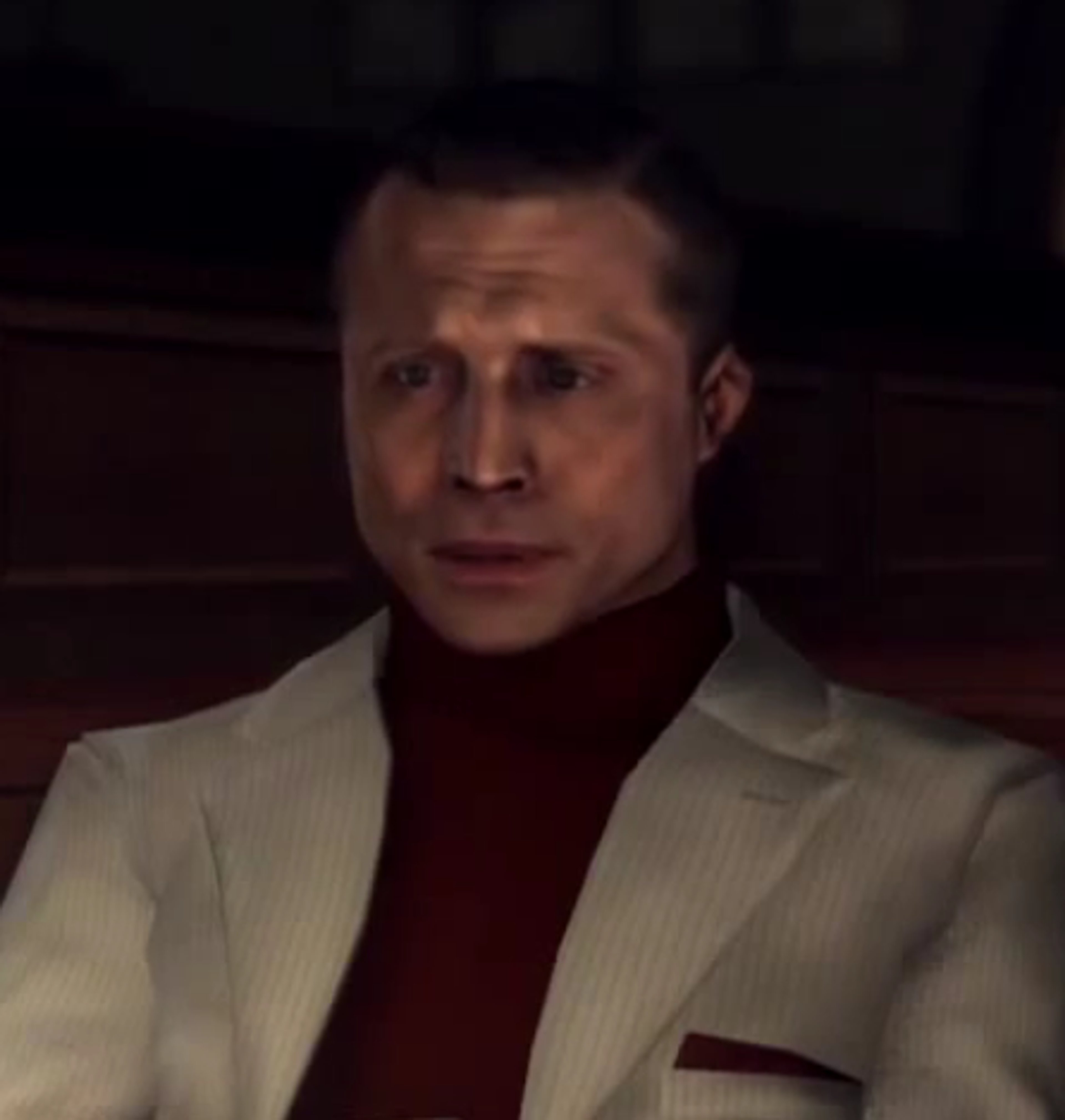 A man in a white suit jacket and red turtleneck sweater with a serious expression on his face.