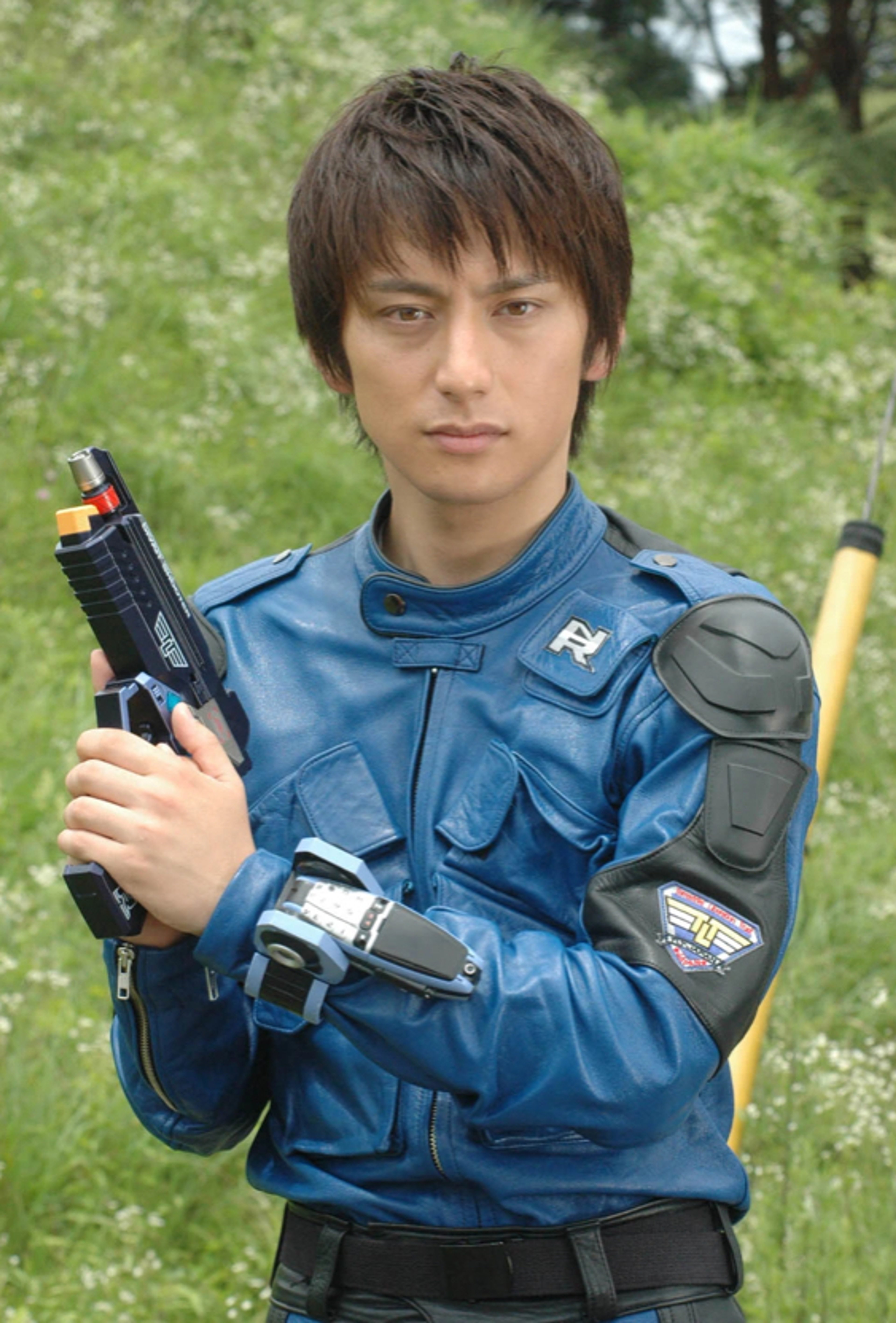 A young man in a blue uniform holding a futuristic gun in a forested setting.