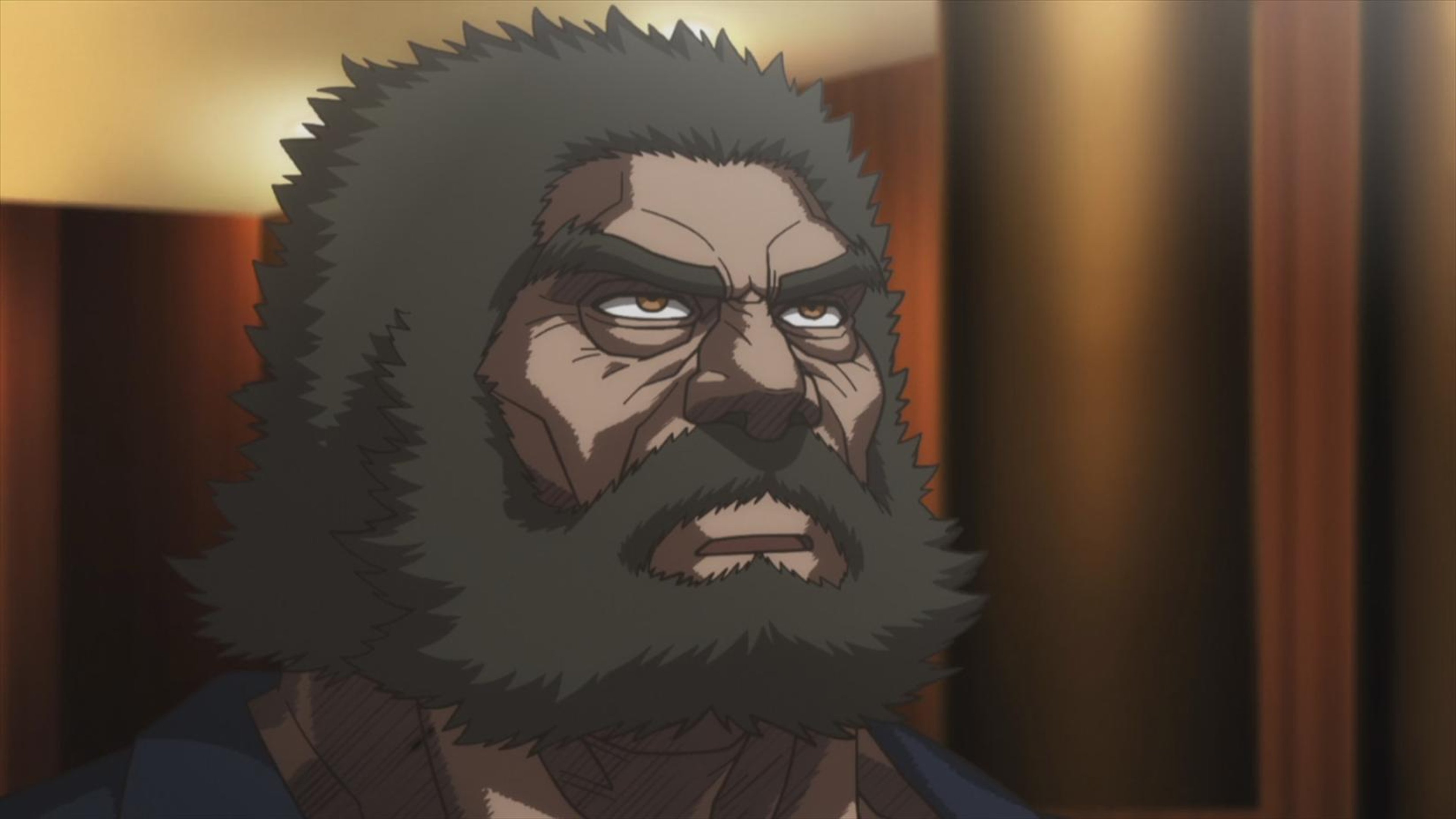 A stern-looking, middle-aged man with a thick beard and long hair, wearing a dark, tattered martial arts-style outfit.