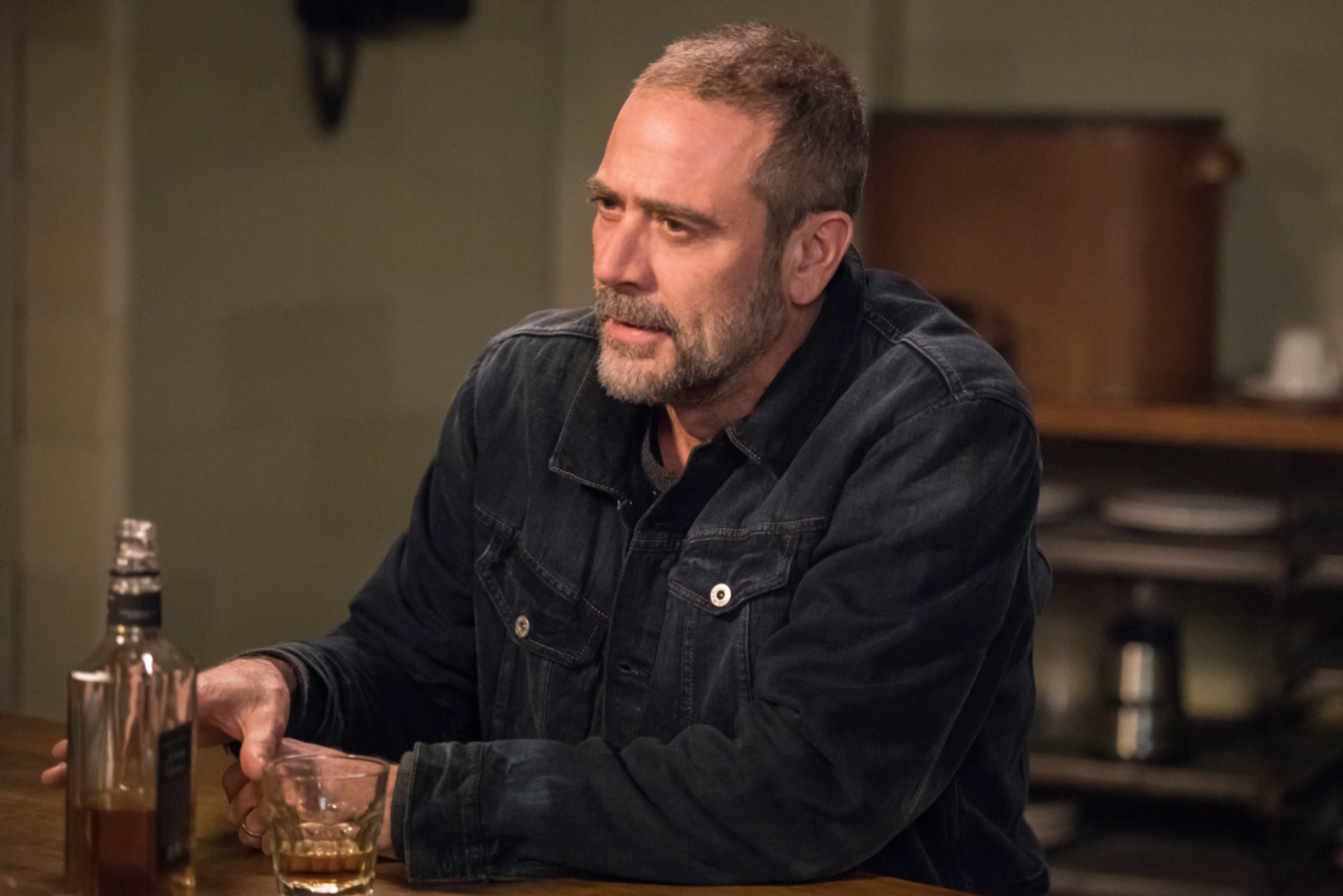 An older man with gray hair and a beard sitting at a table with a drink