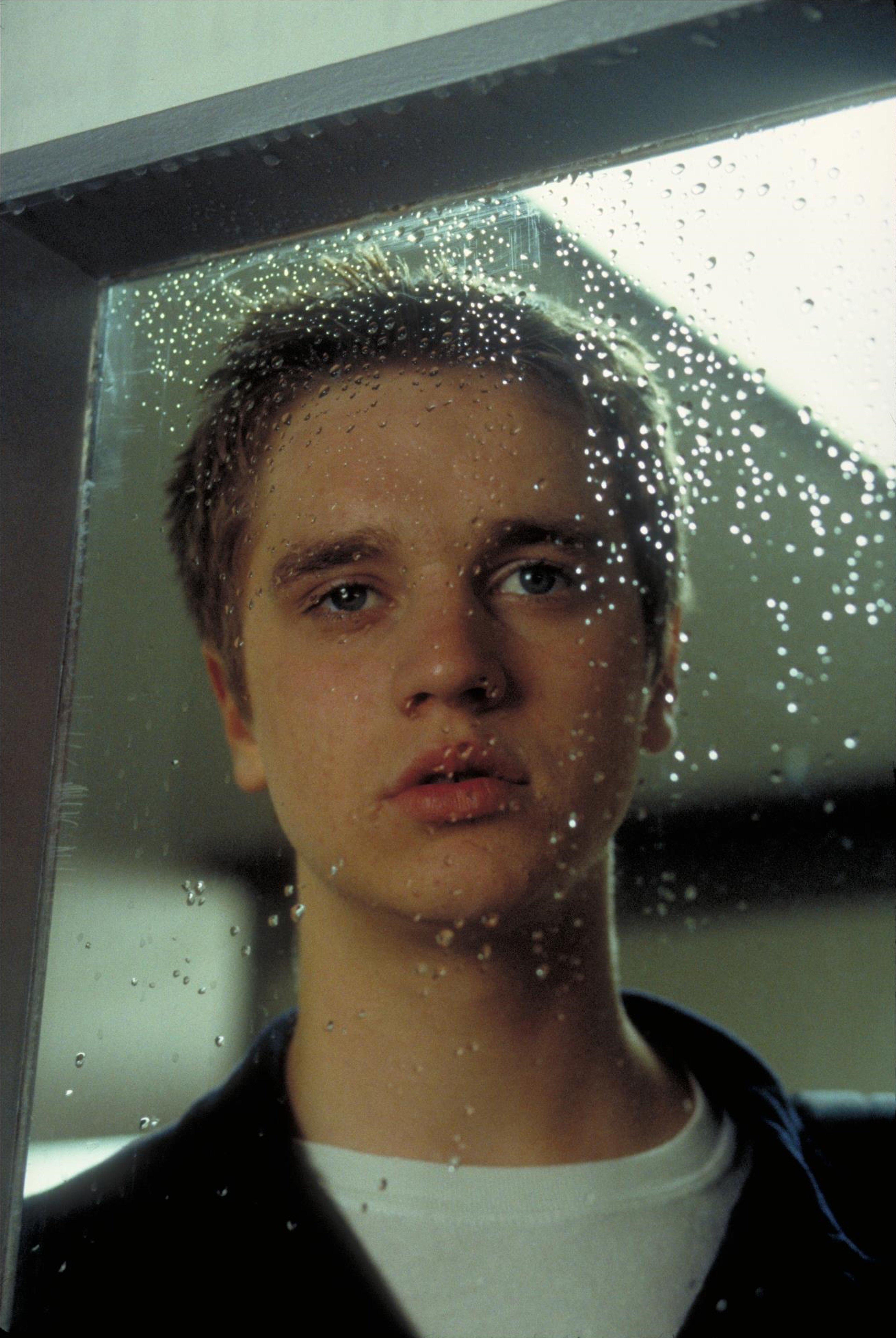 A young man with short brown hair looking serious in a rainy setting