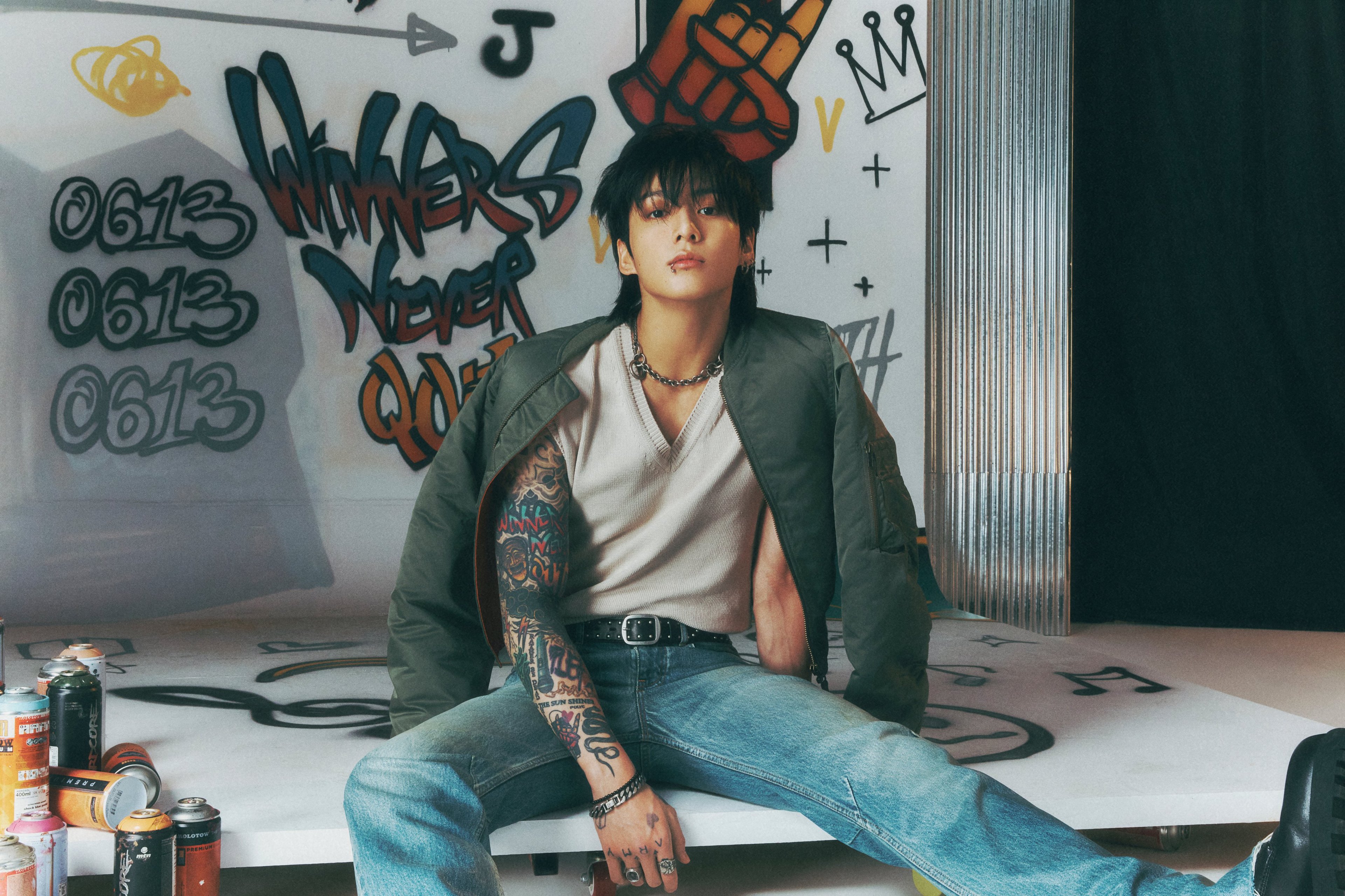 A young man with tattoos sitting at a desk in a graffiti-covered room