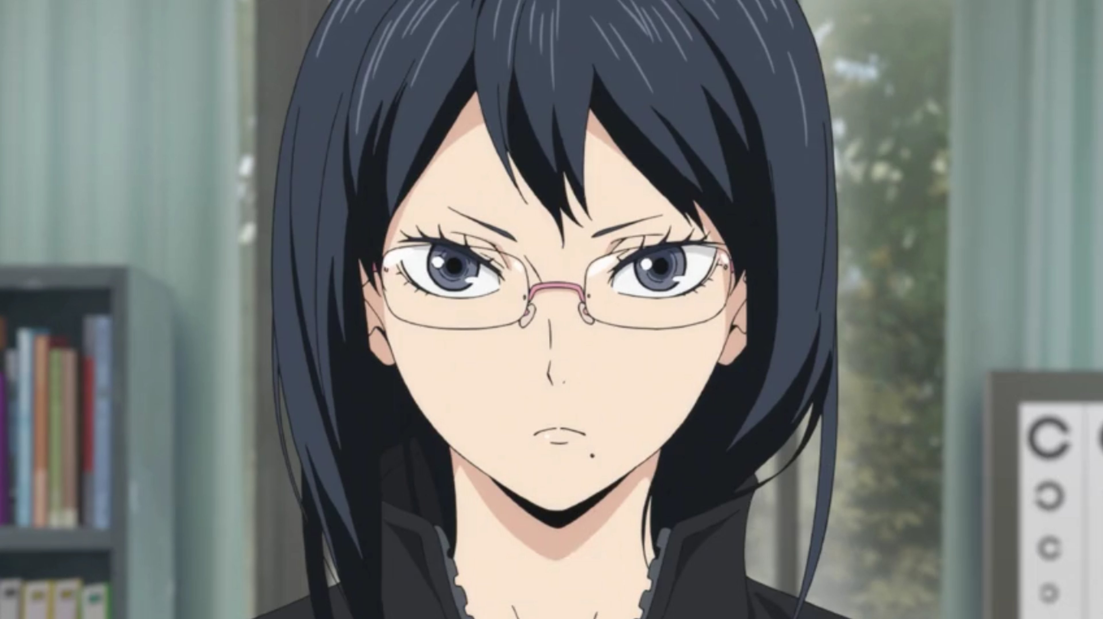 A young woman with black hair and glasses wearing a serious expression