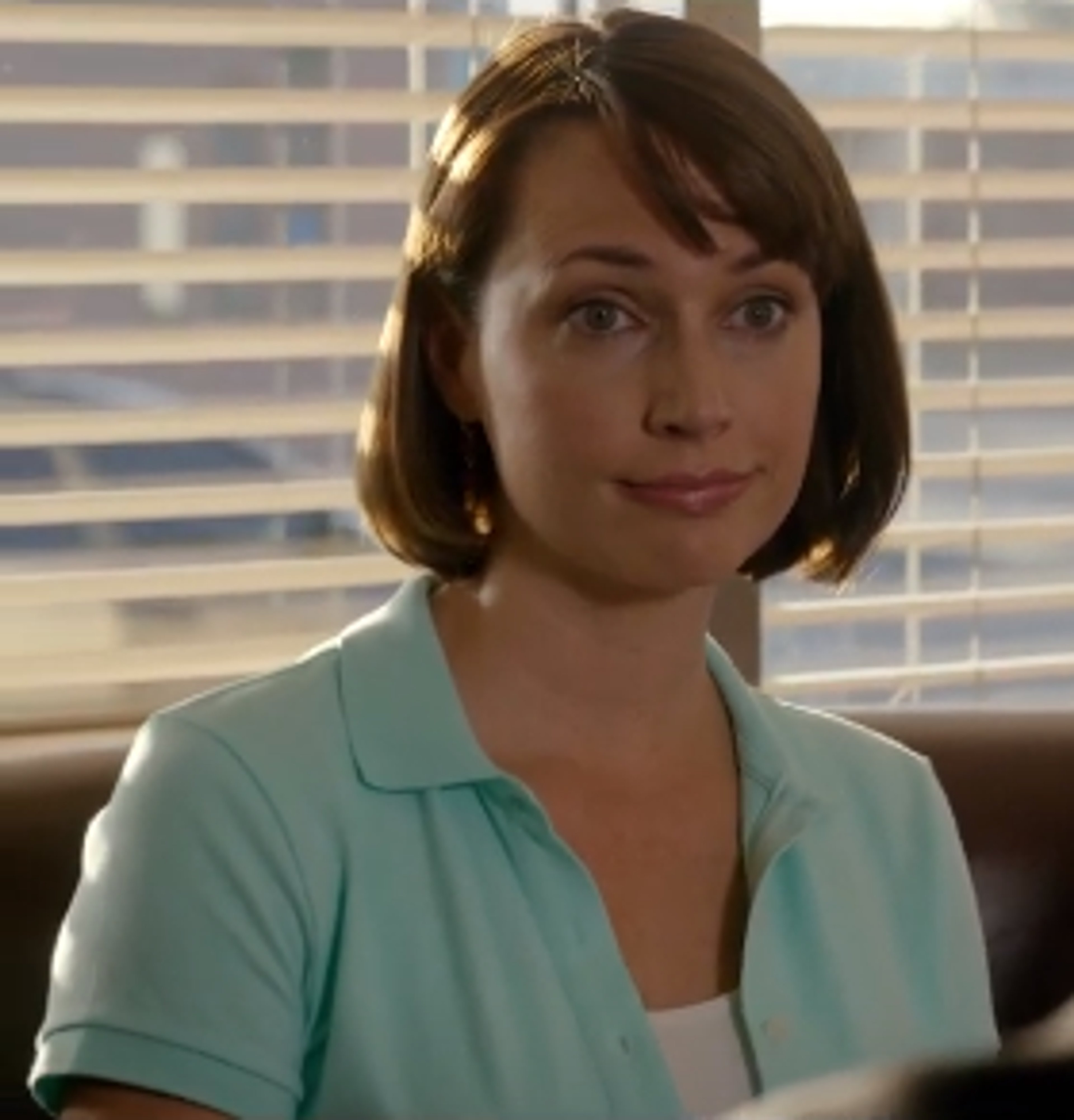 A woman with short brown hair wearing a light blue collared shirt