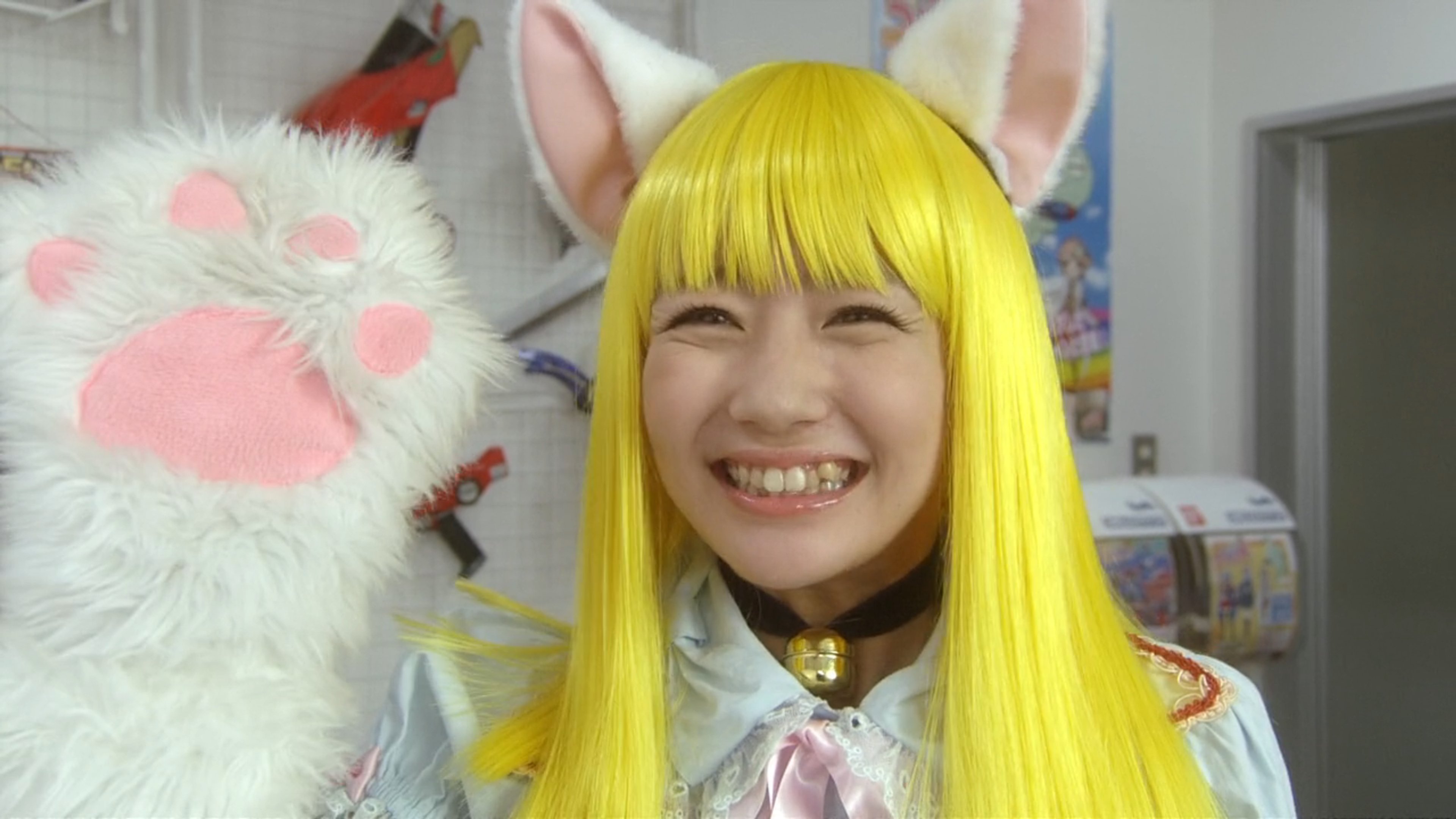 A young woman with bright yellow hair and an anime-inspired costume, smiling cheerfully at the camera.