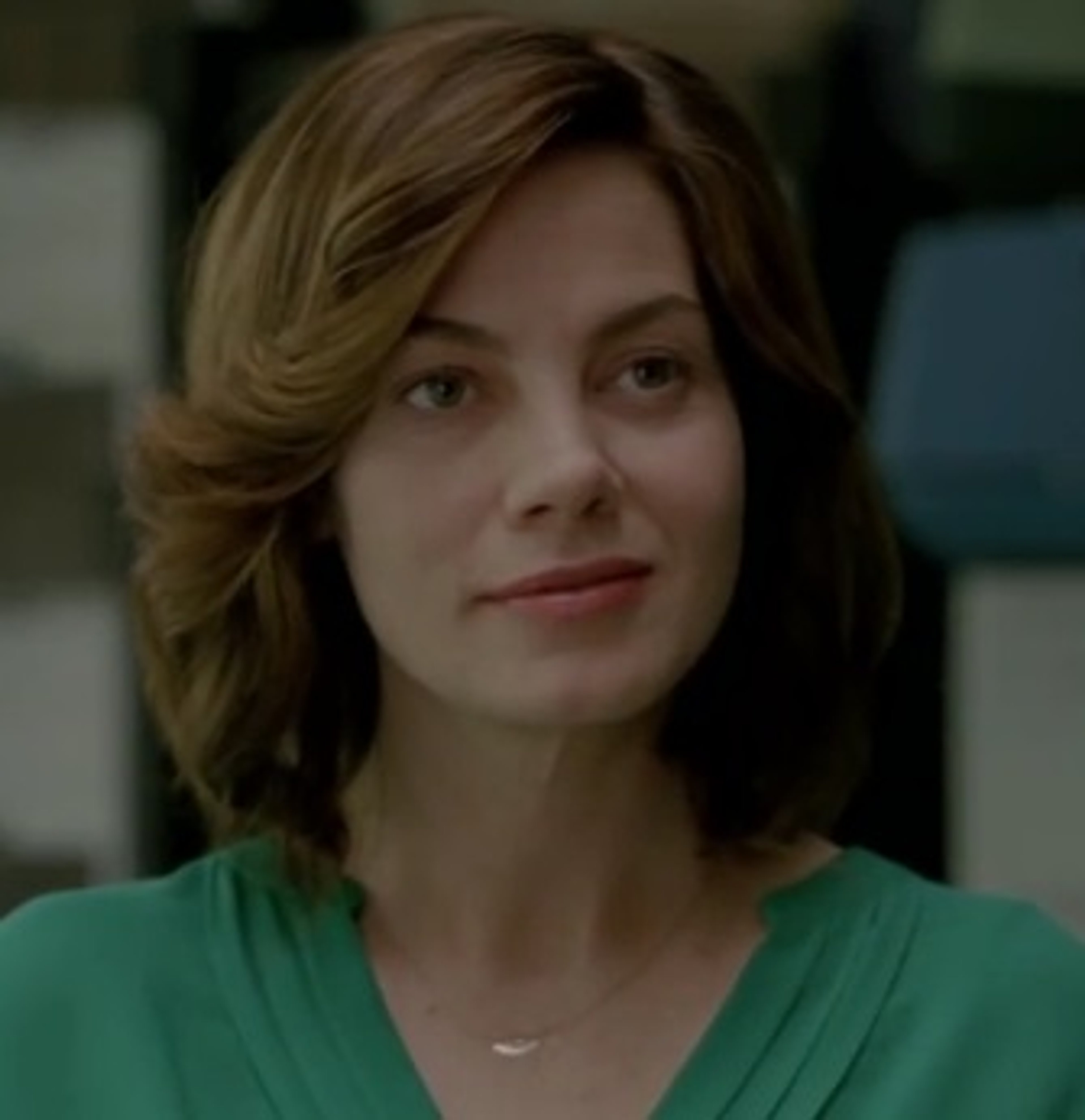 A woman with brown hair and green eyes wearing a green top