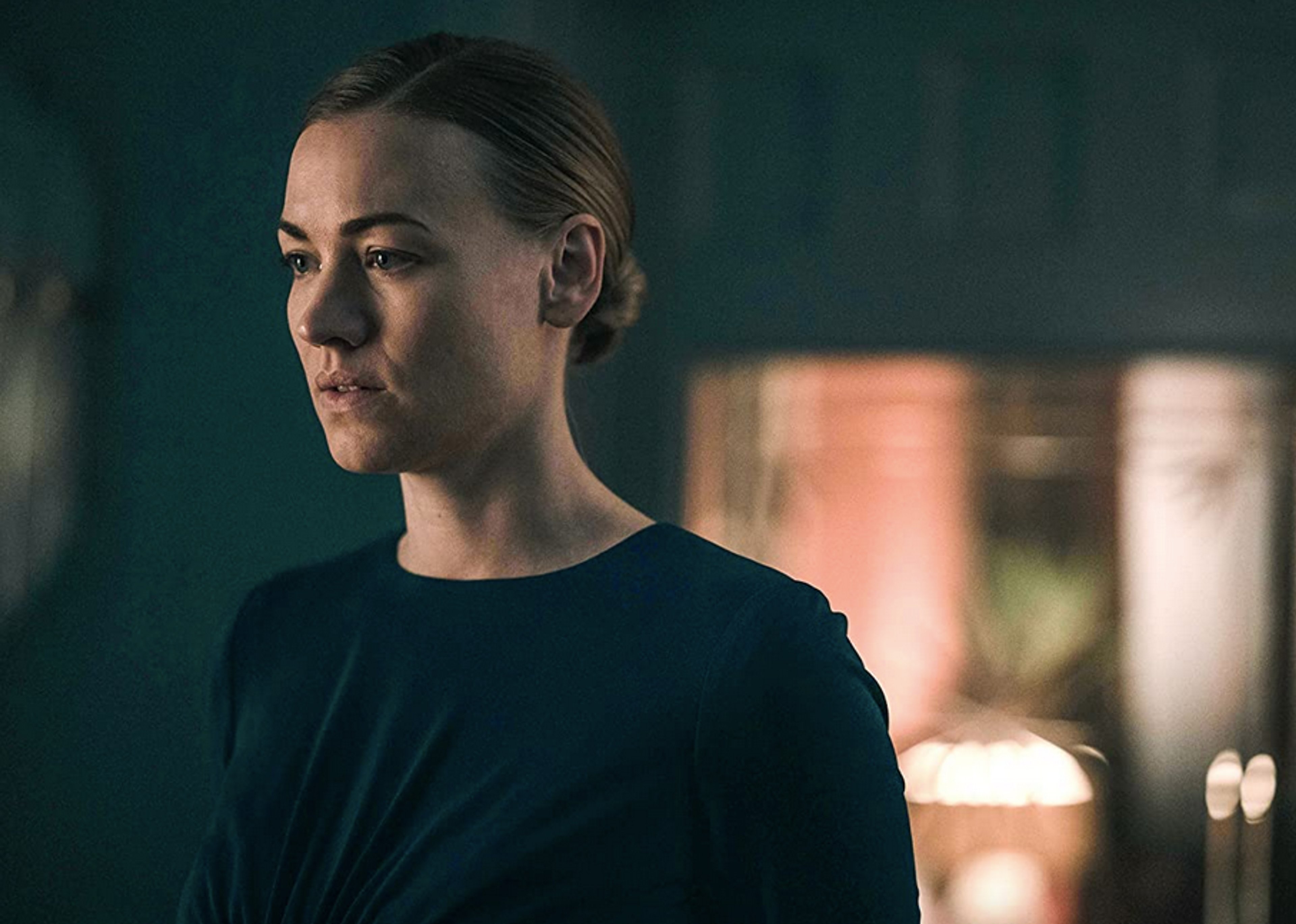 A woman with a serious expression in a dimly lit setting