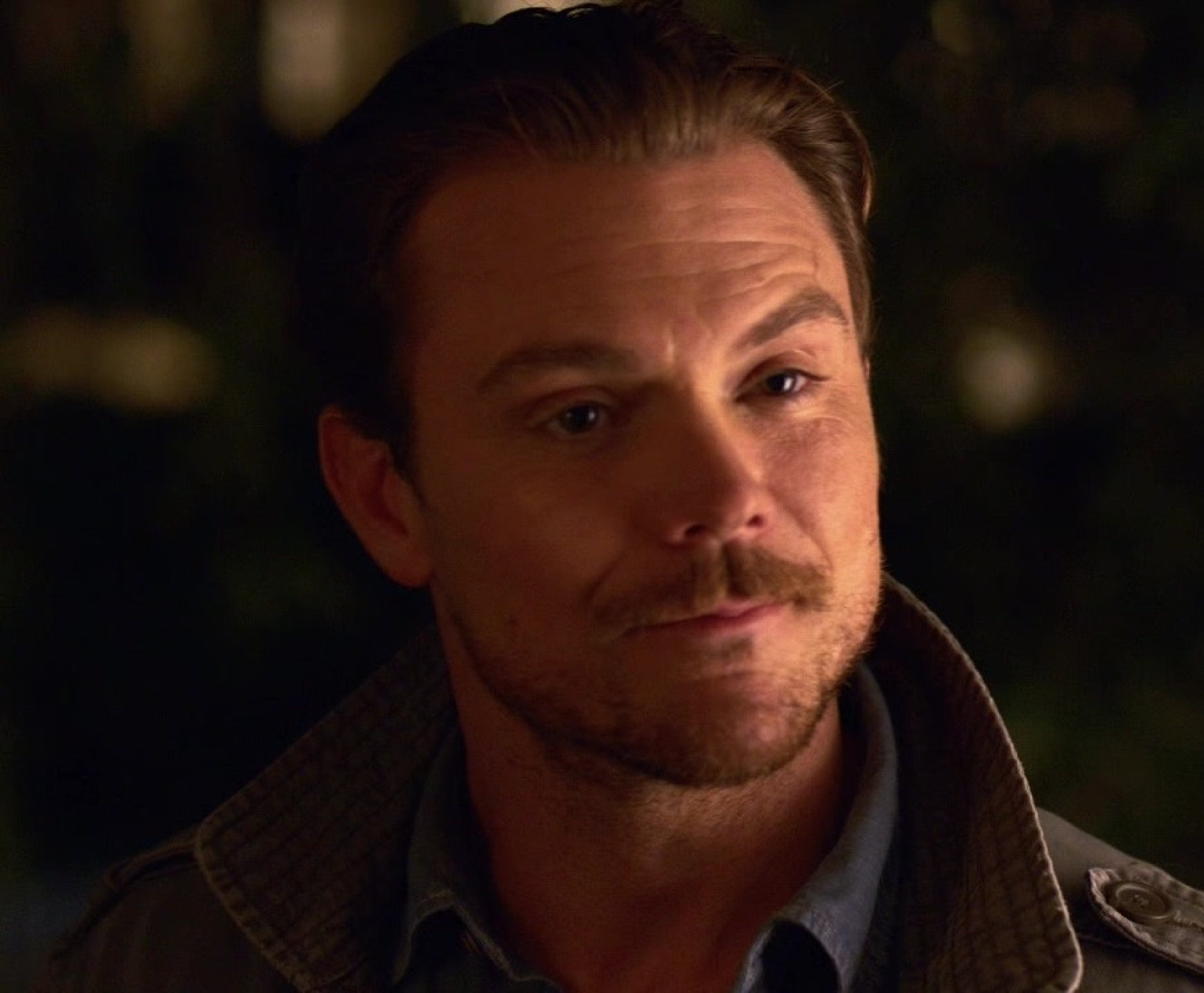 A middle-aged man with a beard and mustache, wearing a dark jacket and shirt, with an intense expression on his face.