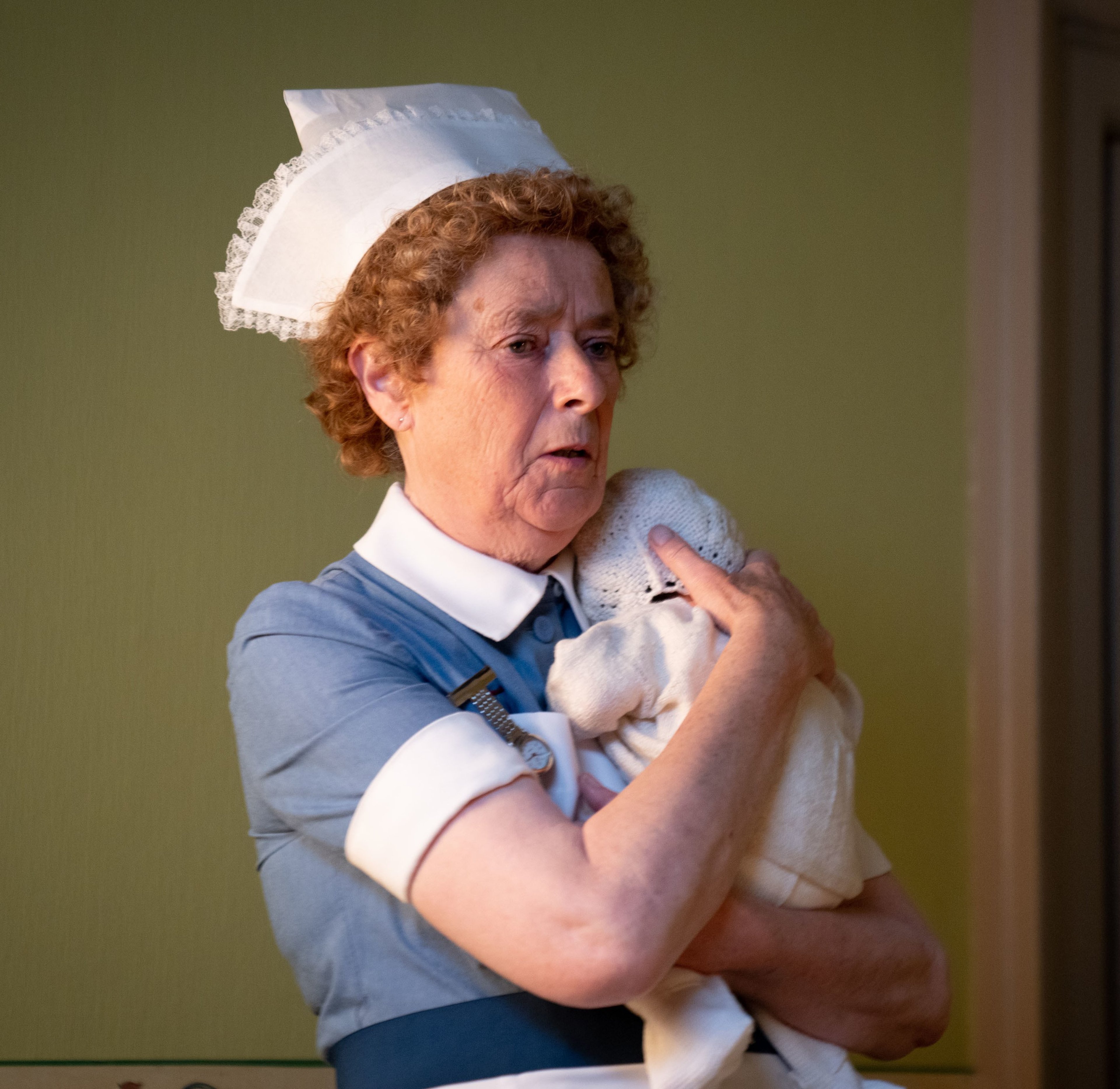 An older woman in a nurse's uniform holding a clipboard