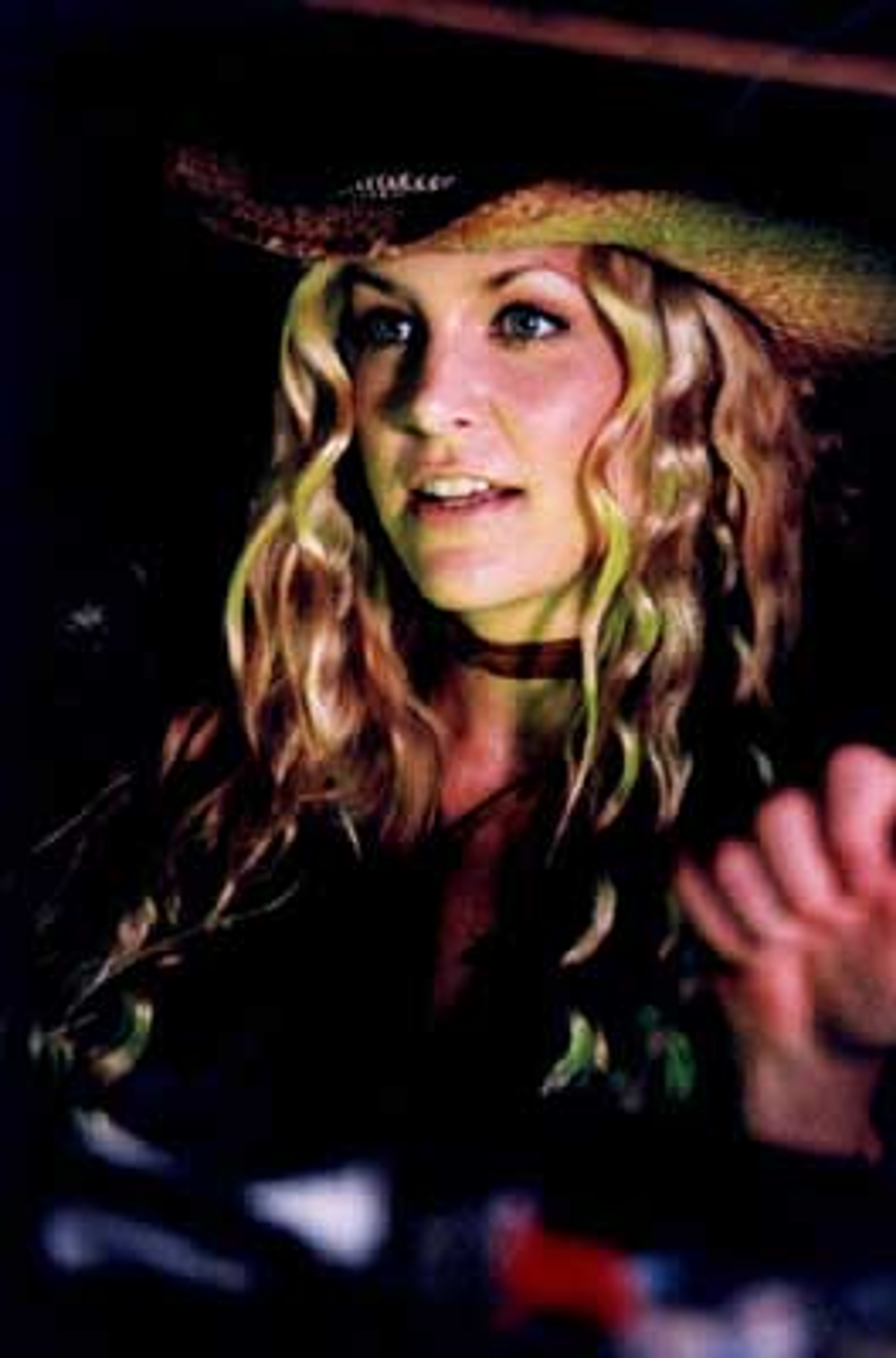 A young woman with curly blonde hair wearing a cowboy hat and smiling at the camera.