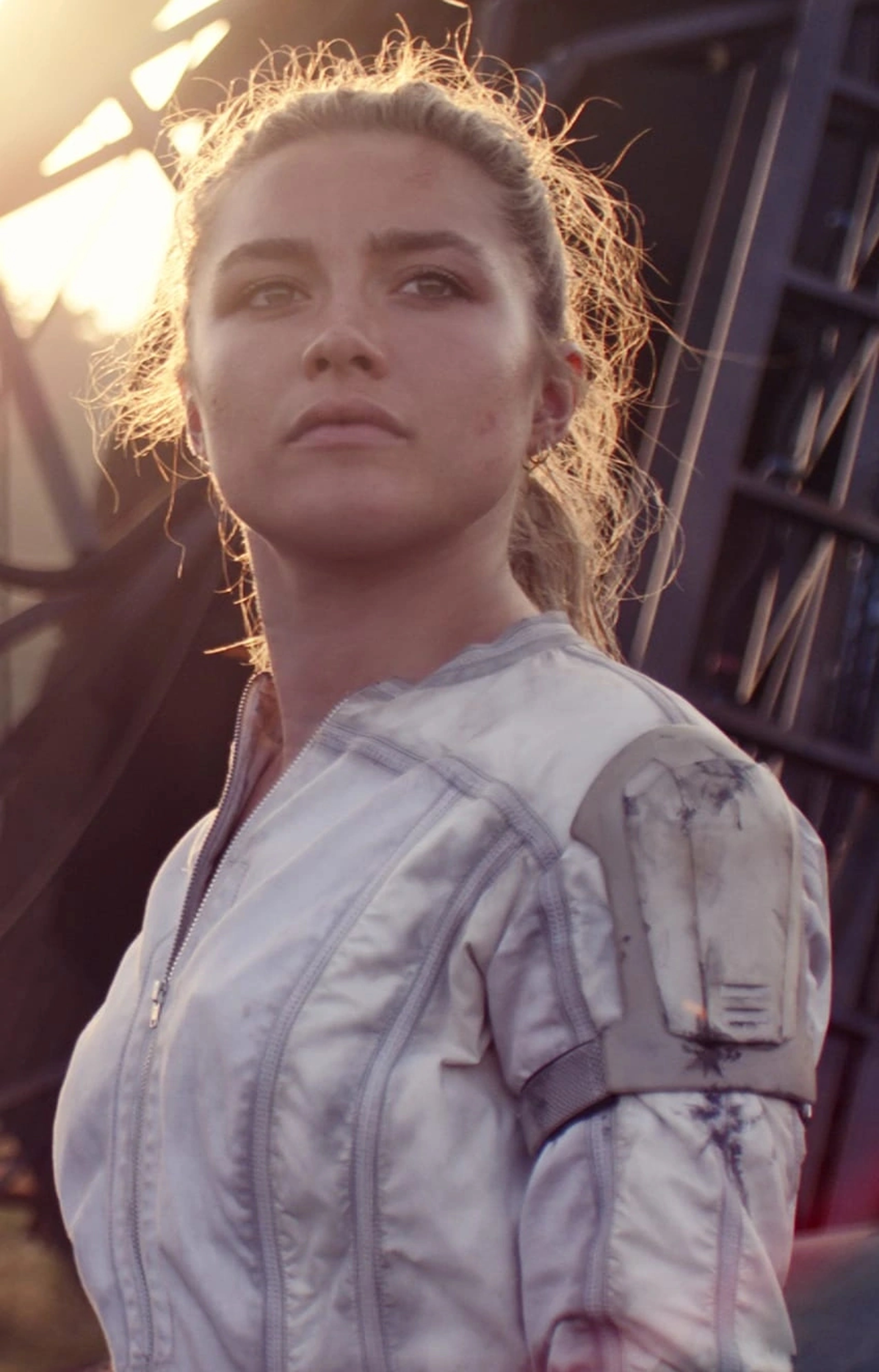 A young woman with blonde hair wearing a white jacket or shirt, looking serious and determined.