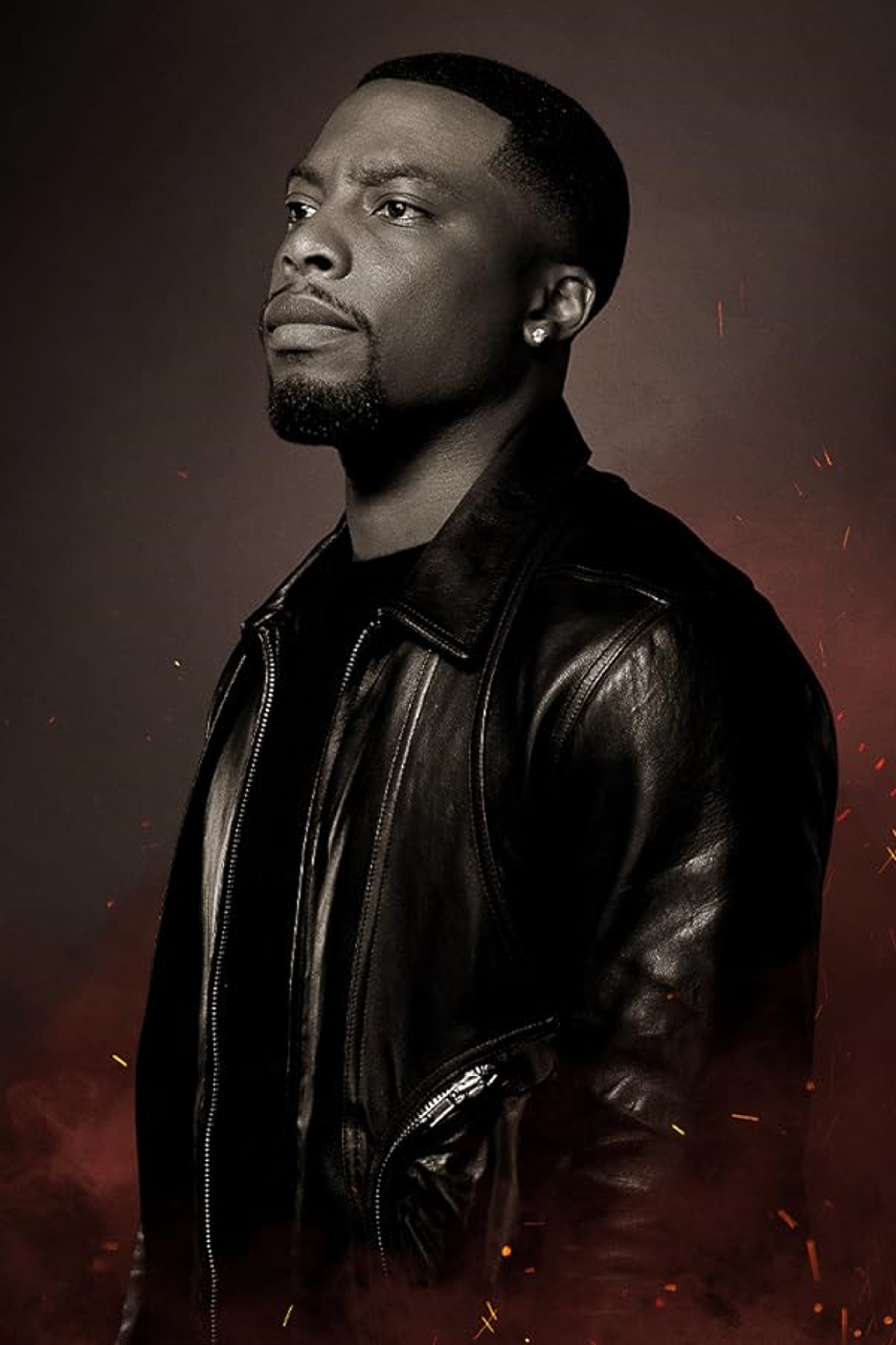 A close-up portrait of a Black man with a serious expression, wearing a black leather jacket.