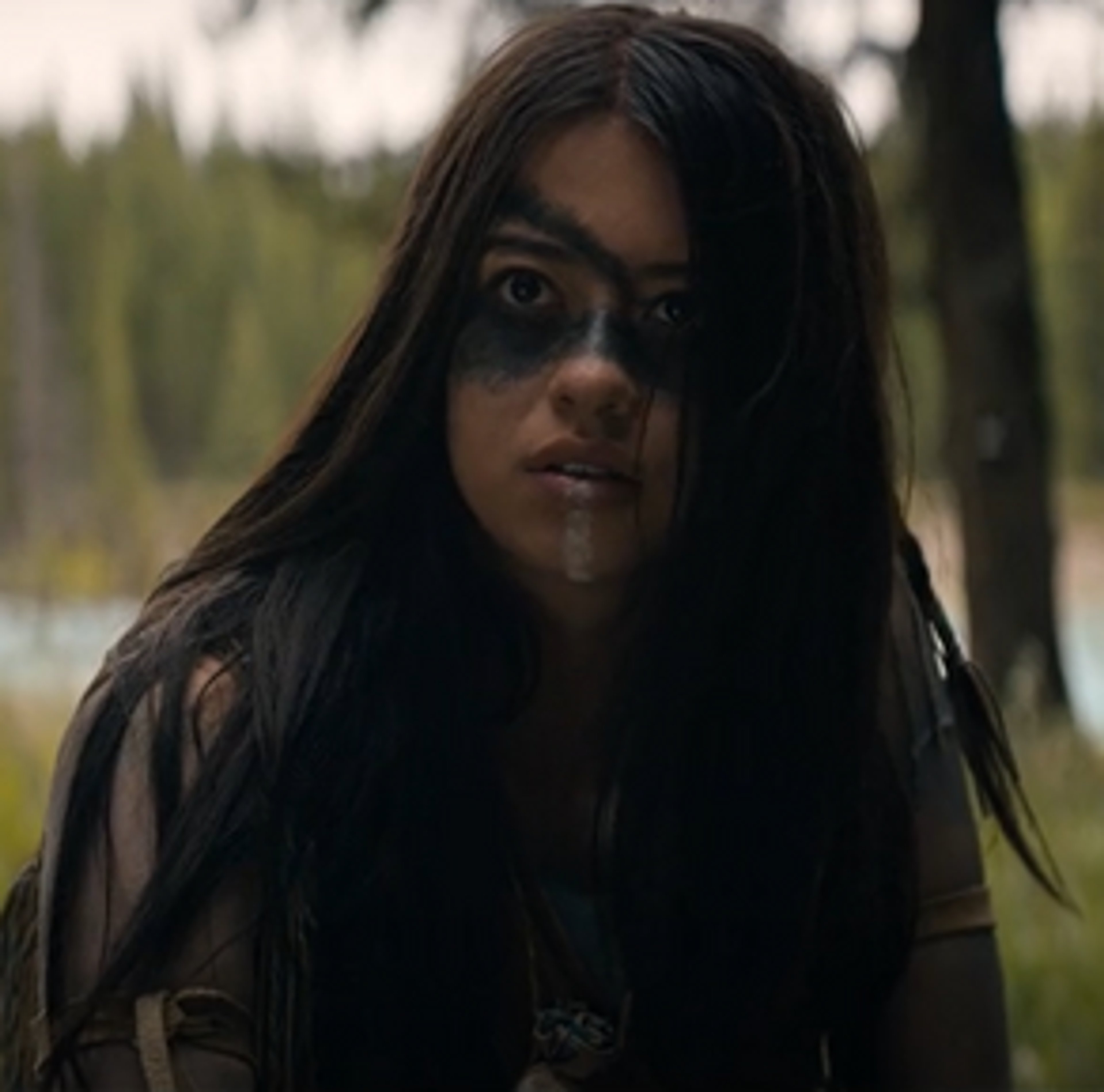 A young Comanche woman with long dark hair standing in a natural outdoor setting