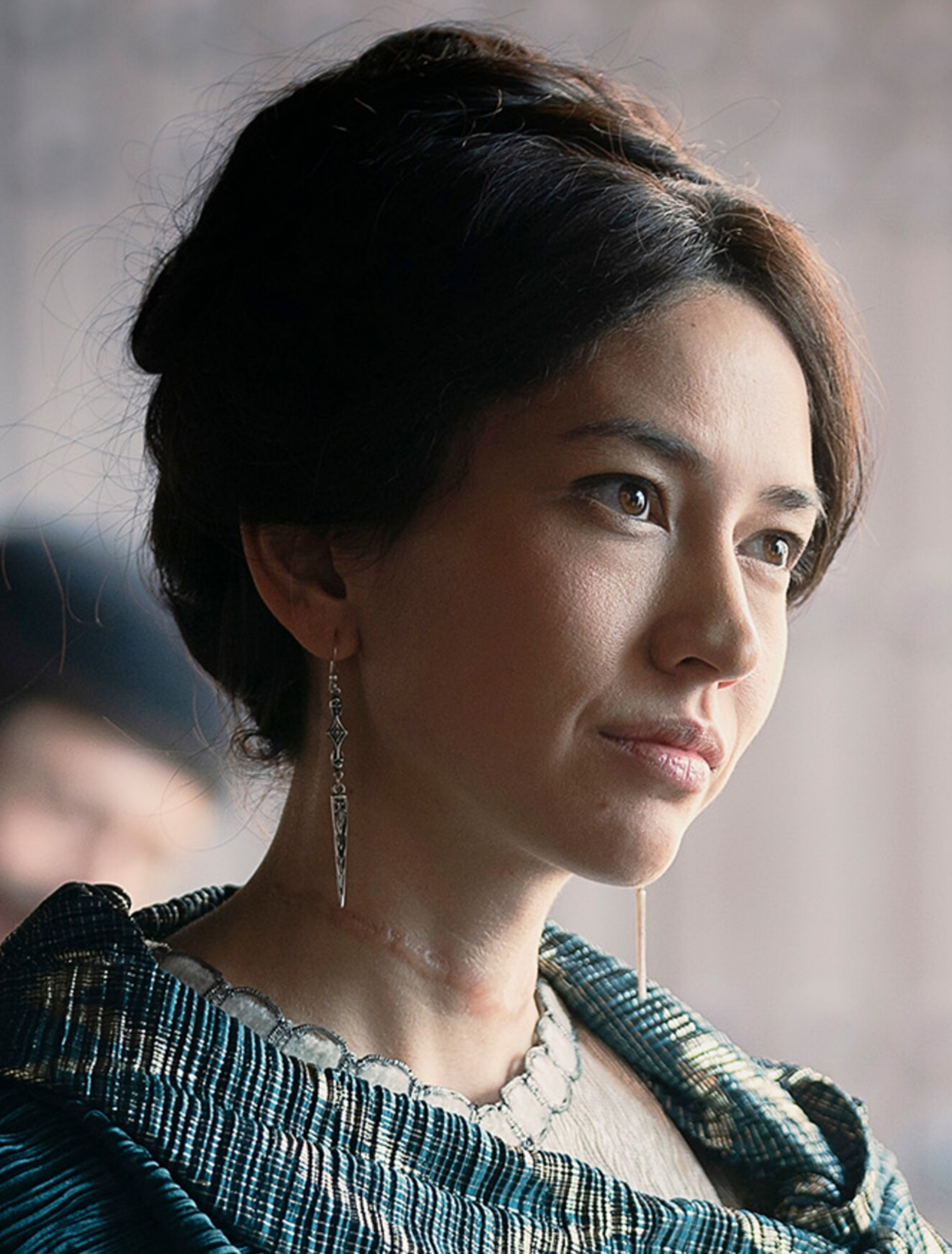 A woman with dark hair and a serious expression, wearing a patterned dress.