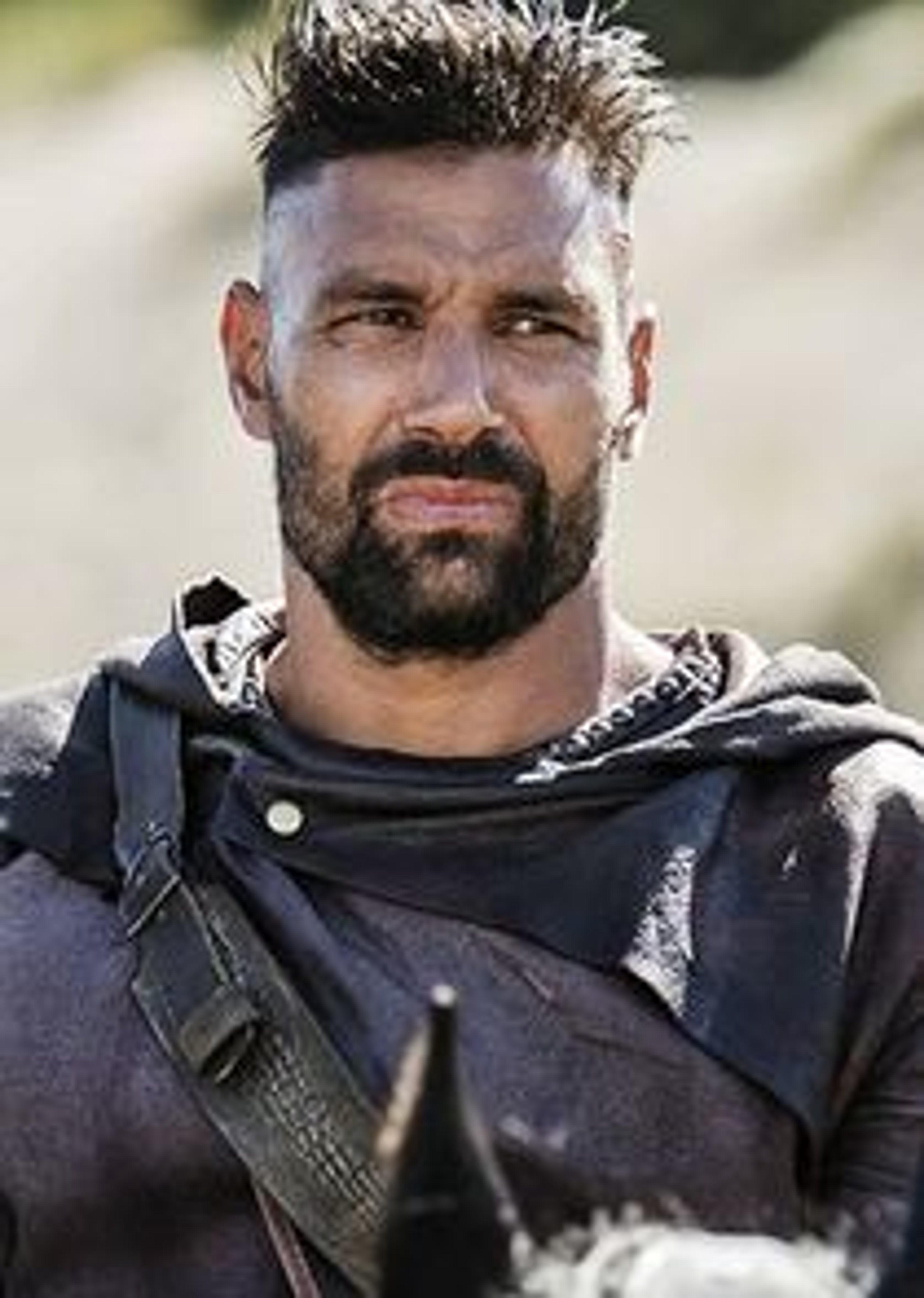 A man with a rugged, bearded appearance in an outdoor setting