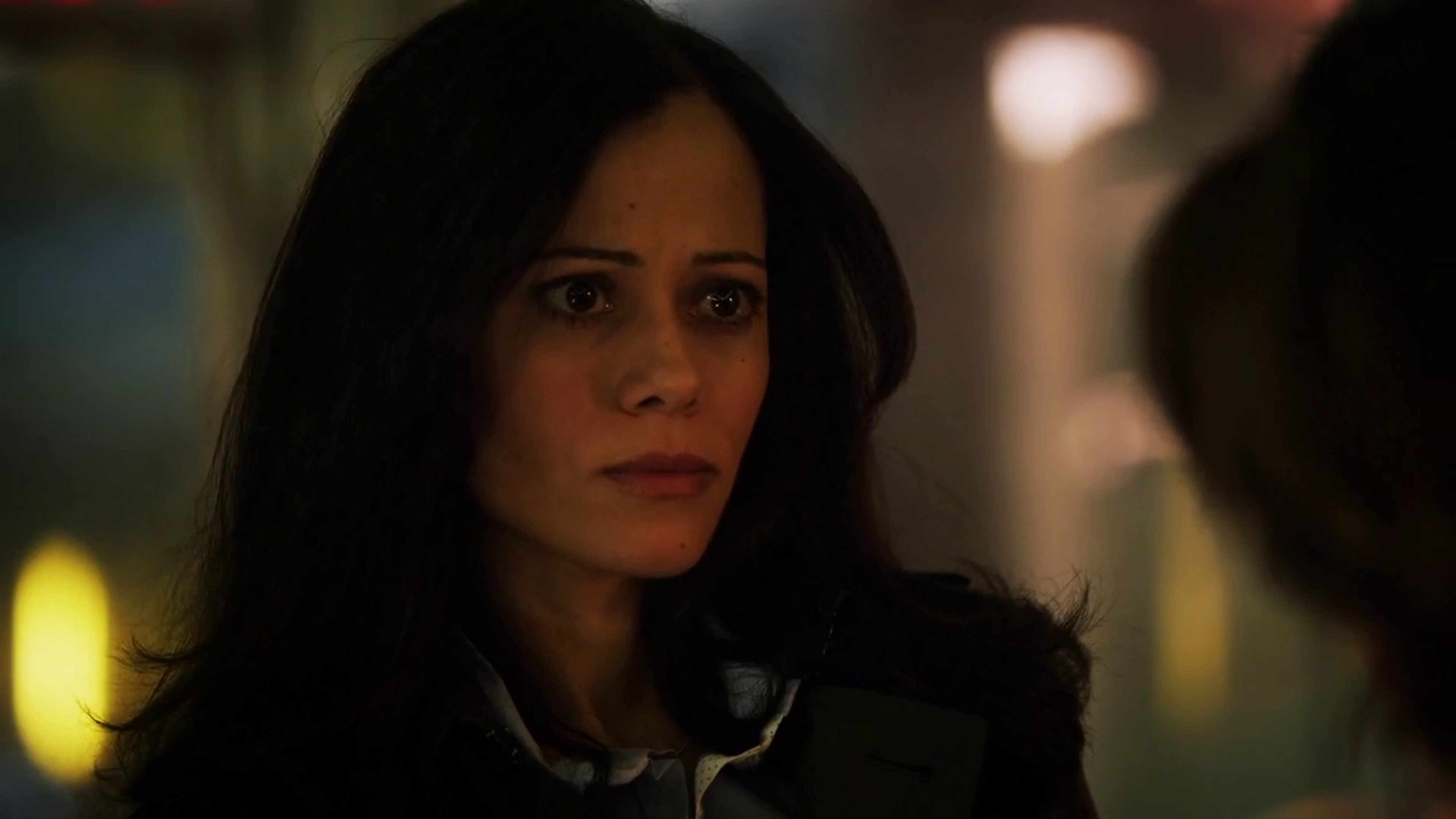 A woman with dark hair and a serious expression, wearing a dark jacket or coat.