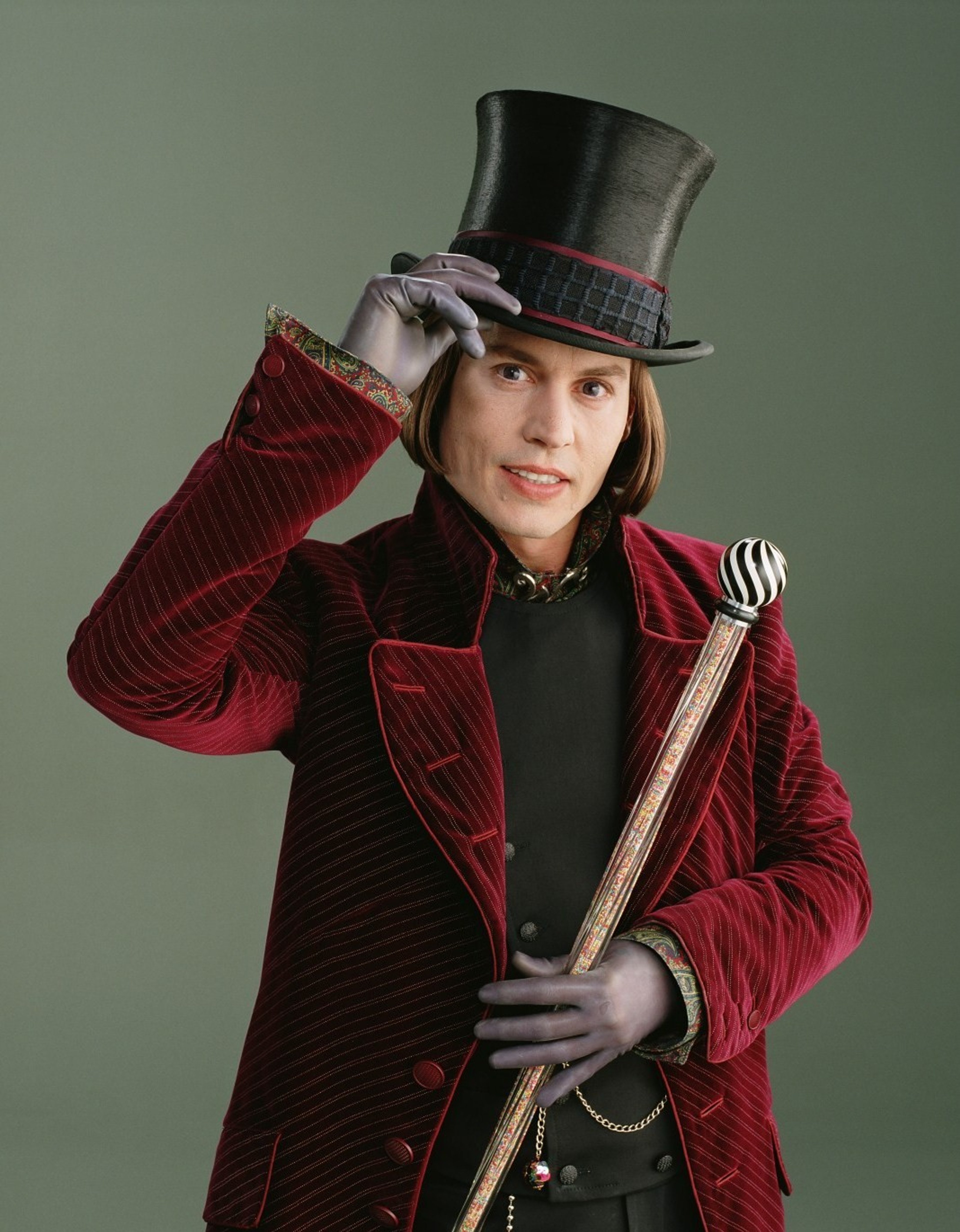 A man in a red velvet coat and top hat, holding a cane and smiling
