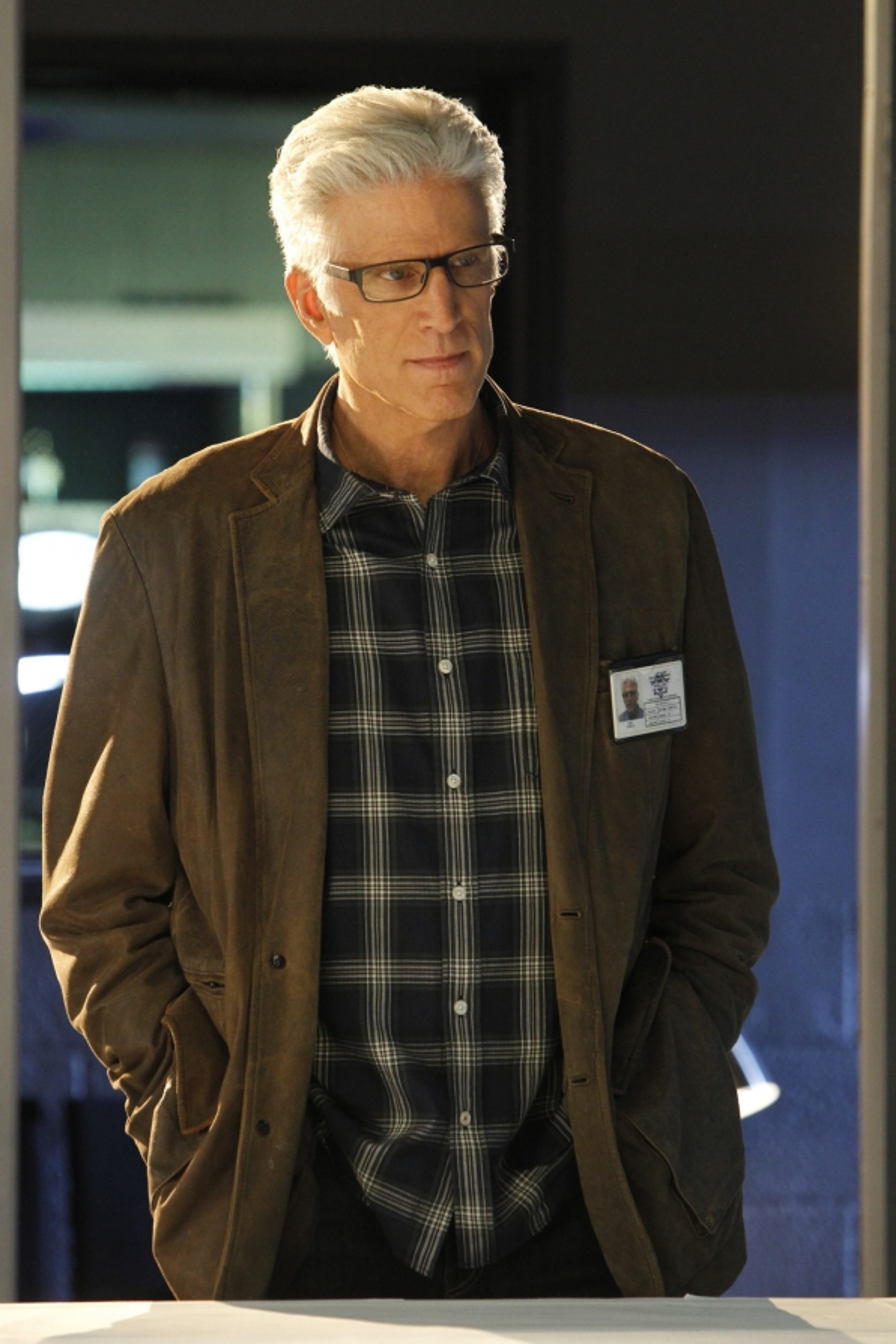 A middle-aged man with gray hair and glasses, wearing a plaid shirt and brown jacket, in a professional setting.