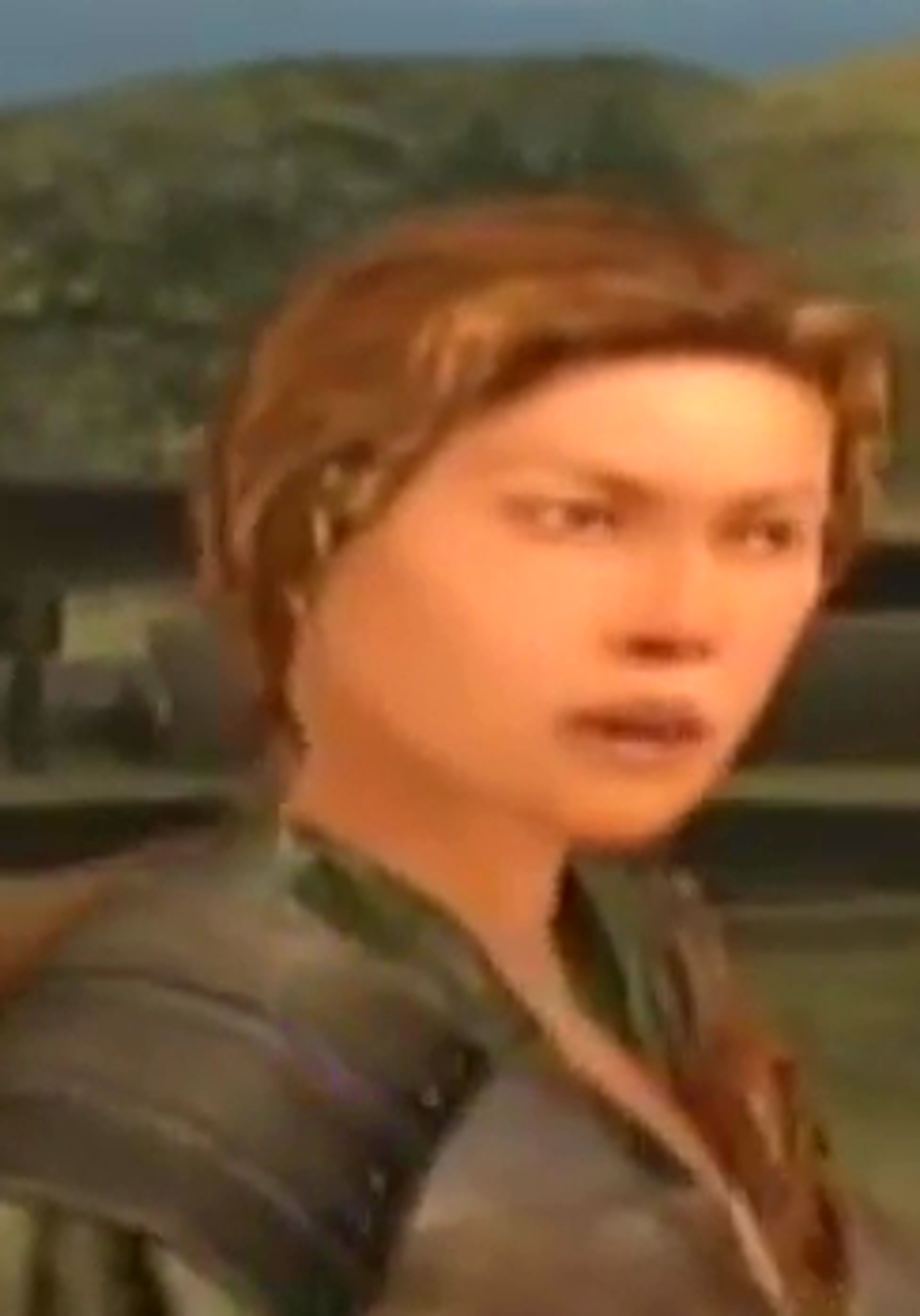 A young woman with long brown hair wearing a green and brown outfit, with a determined expression on her face.
