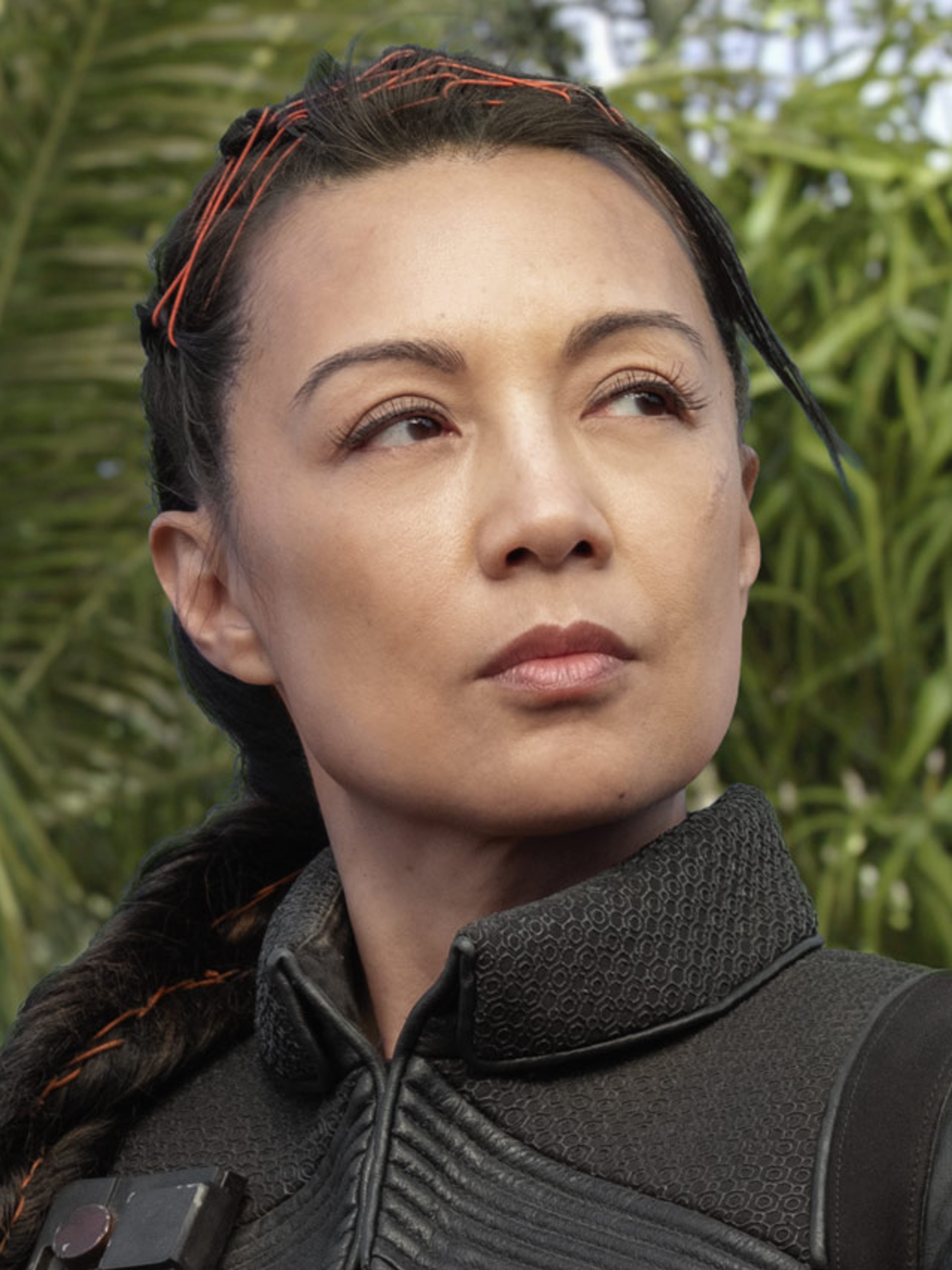 A woman with dark hair in a braid, wearing a black outfit with a high collar, looking serious and focused.