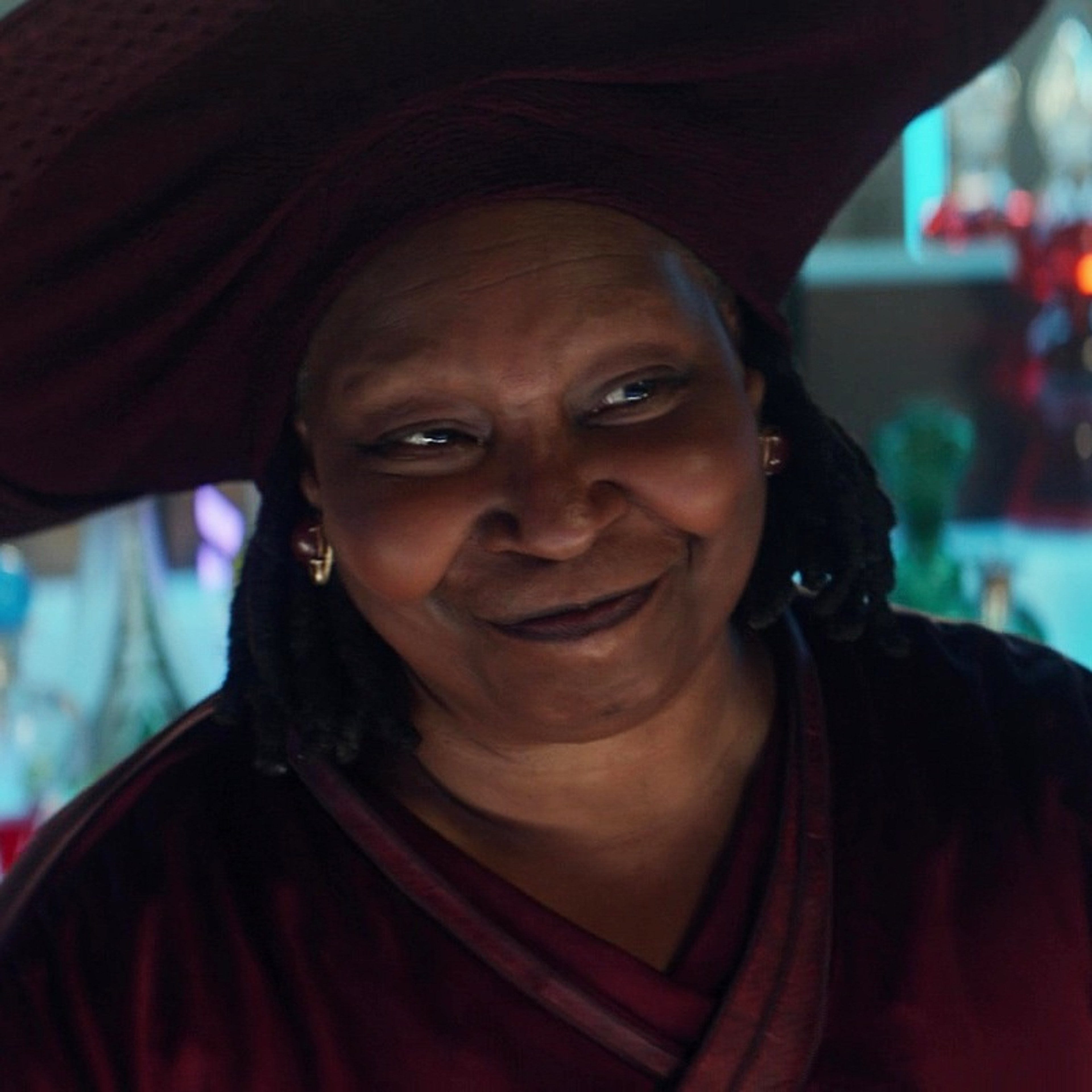A smiling older woman wearing a large hat and flowing robes