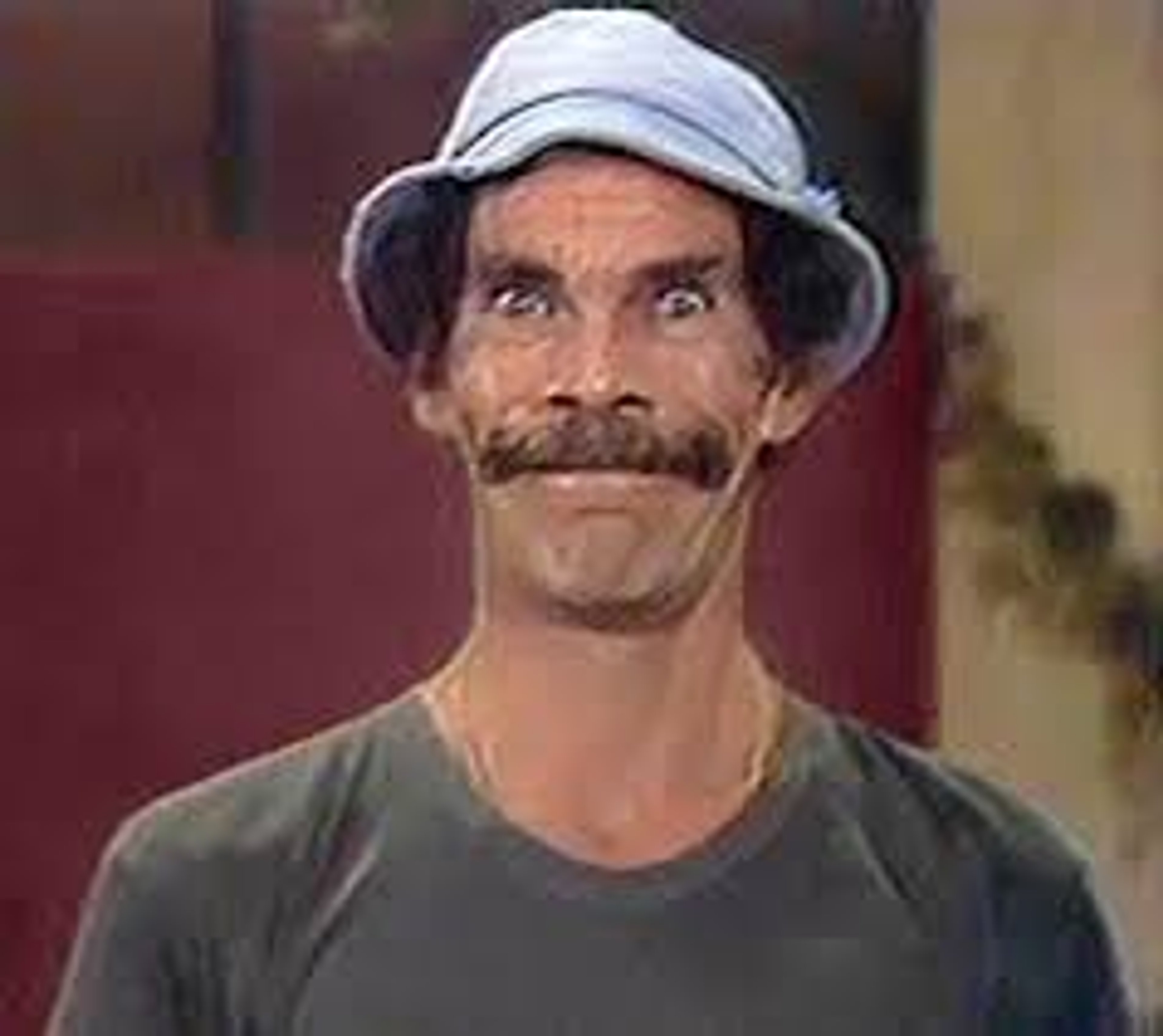 A middle-aged man with a mustache and gruff appearance, wearing a gray hat and green shirt.