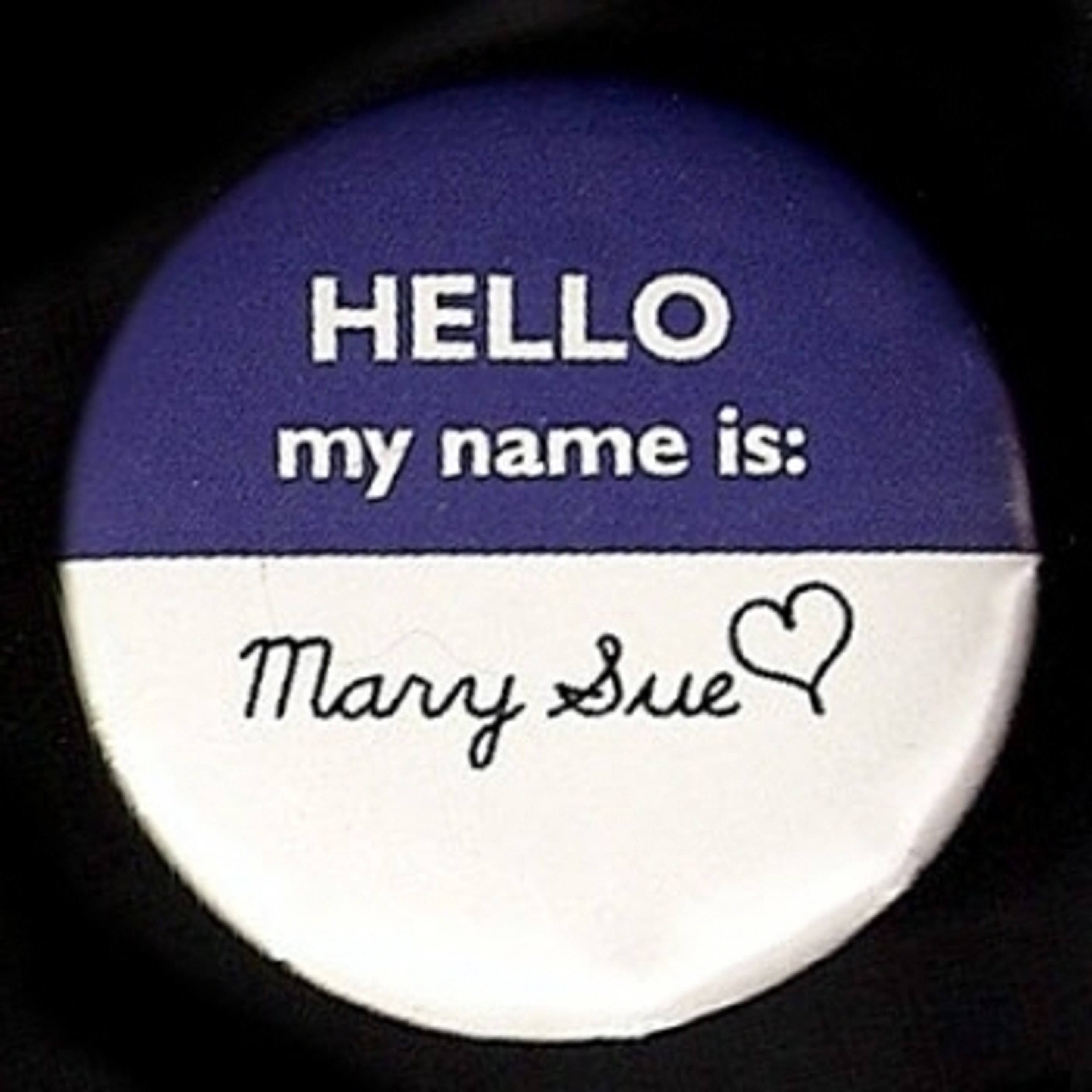 A close-up of a name tag that says 'HELLO my name is: Mary Sue' with a heart symbol next to the name.