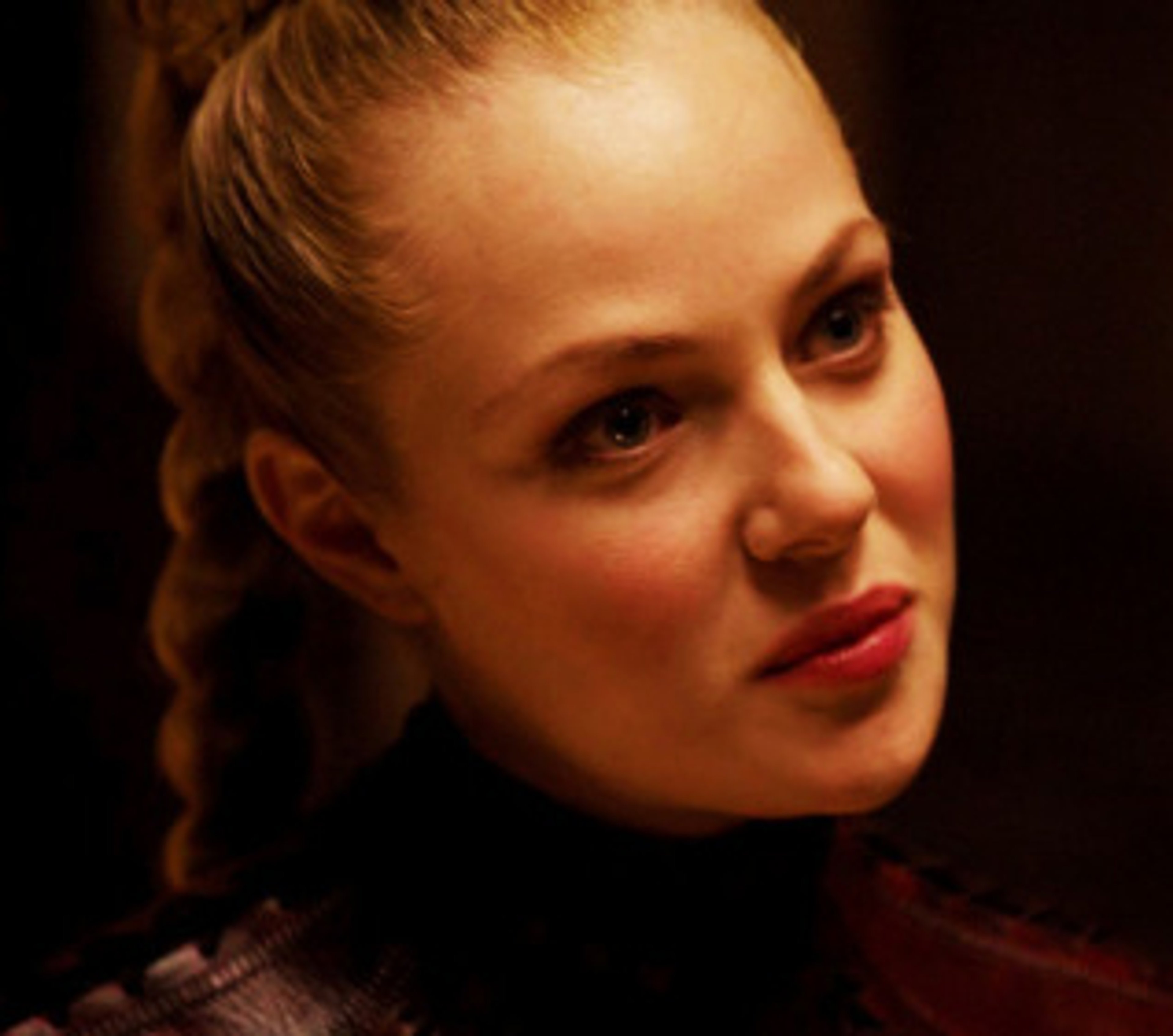 A woman with blonde hair and piercing blue eyes, wearing a red leather outfit.