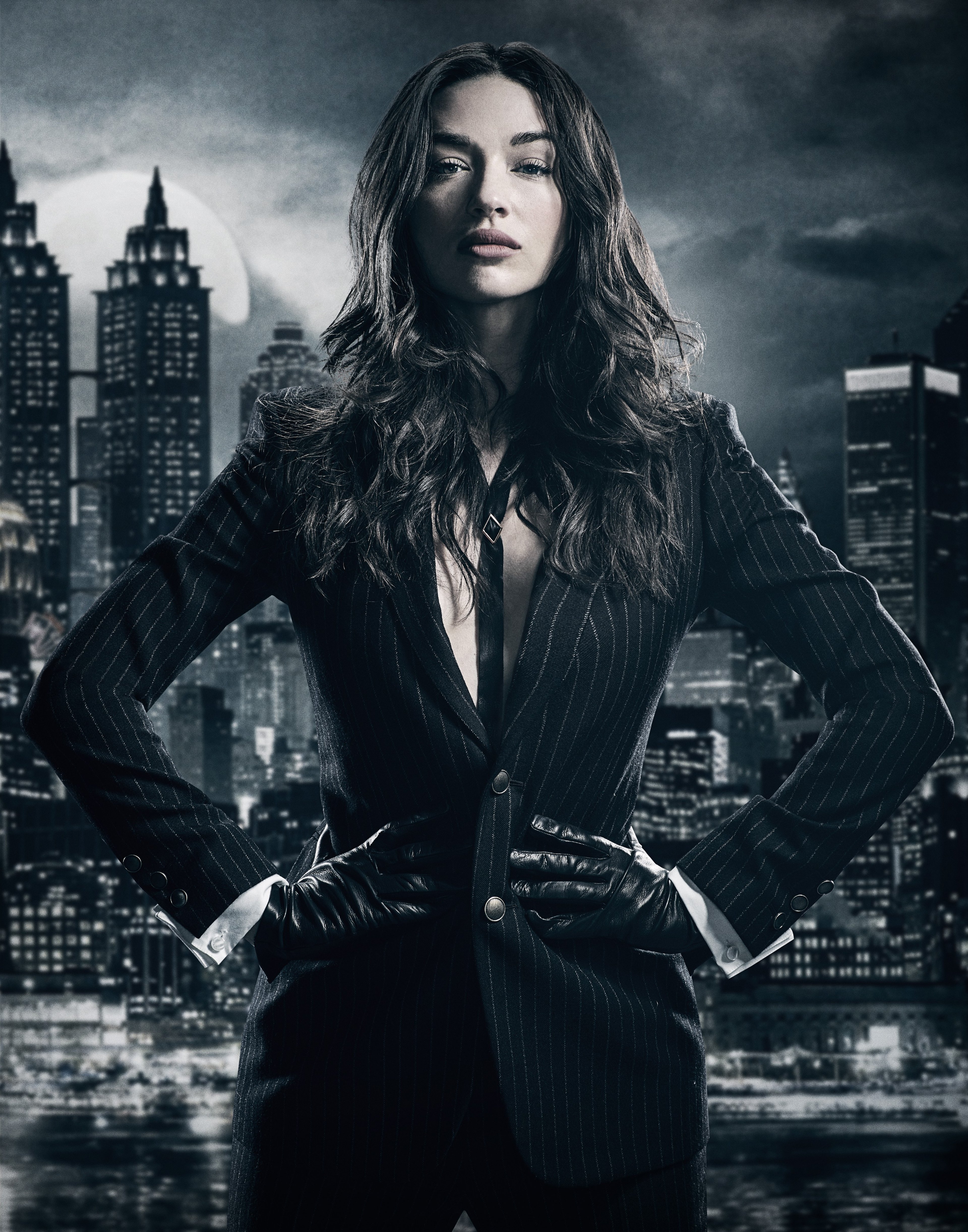 A woman in a black leather jacket standing in front of a city skyline at night