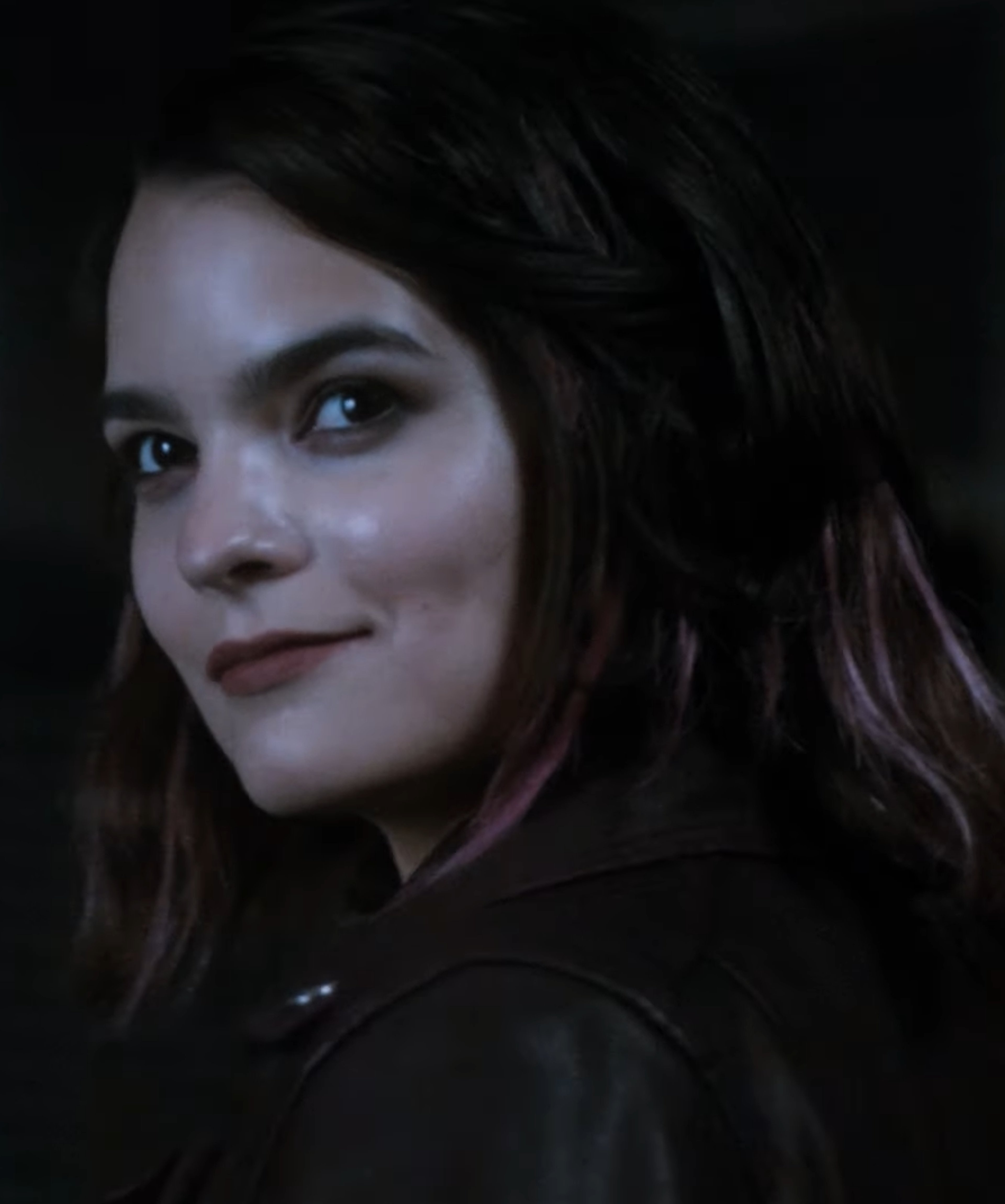 A young woman with dark hair and blue eyes wearing a dark jacket or coat, with a serious expression on her face.