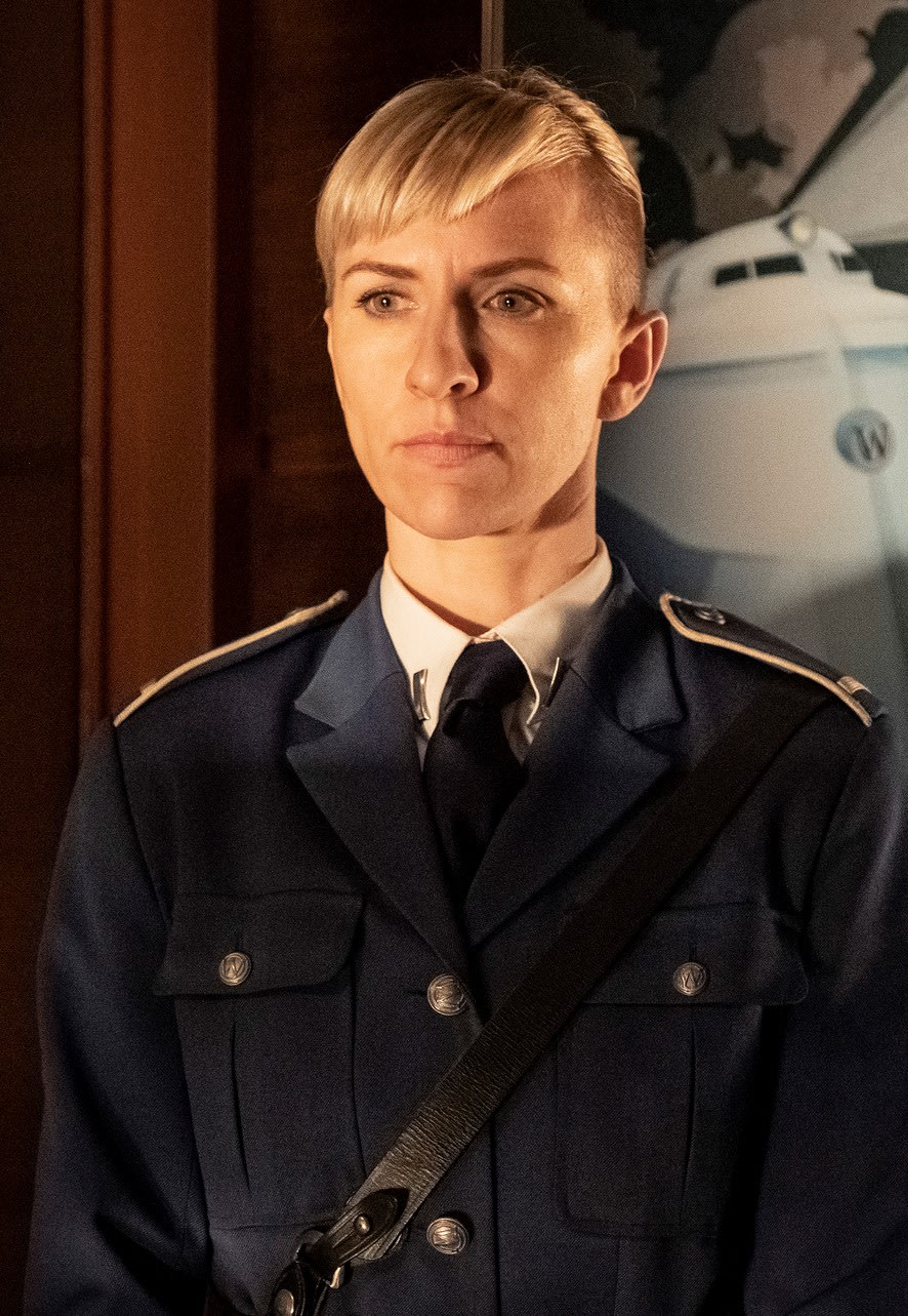 A woman in a dark military-style uniform with a serious expression