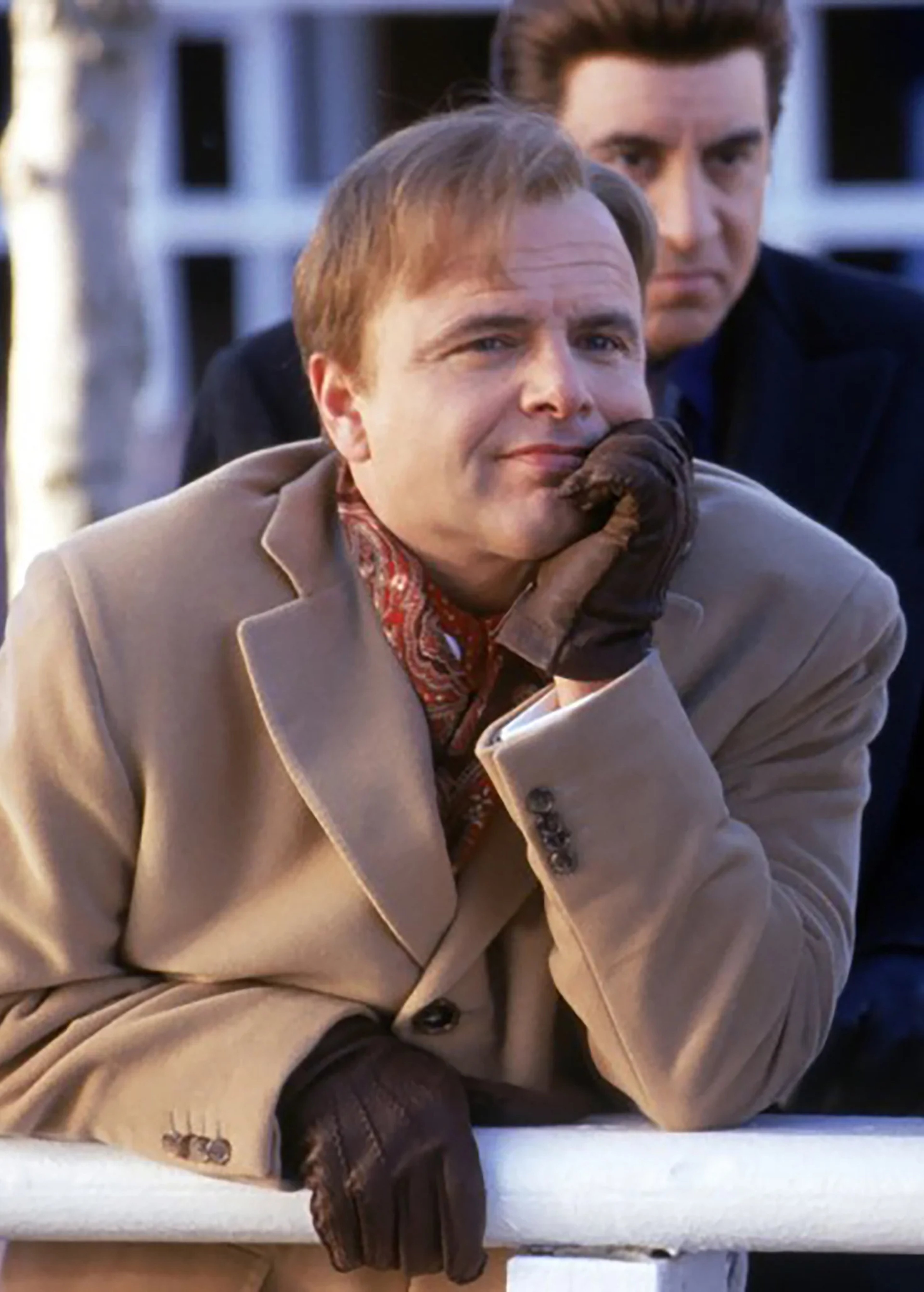 A middle-aged man with a serious expression, wearing a tan coat and scarf