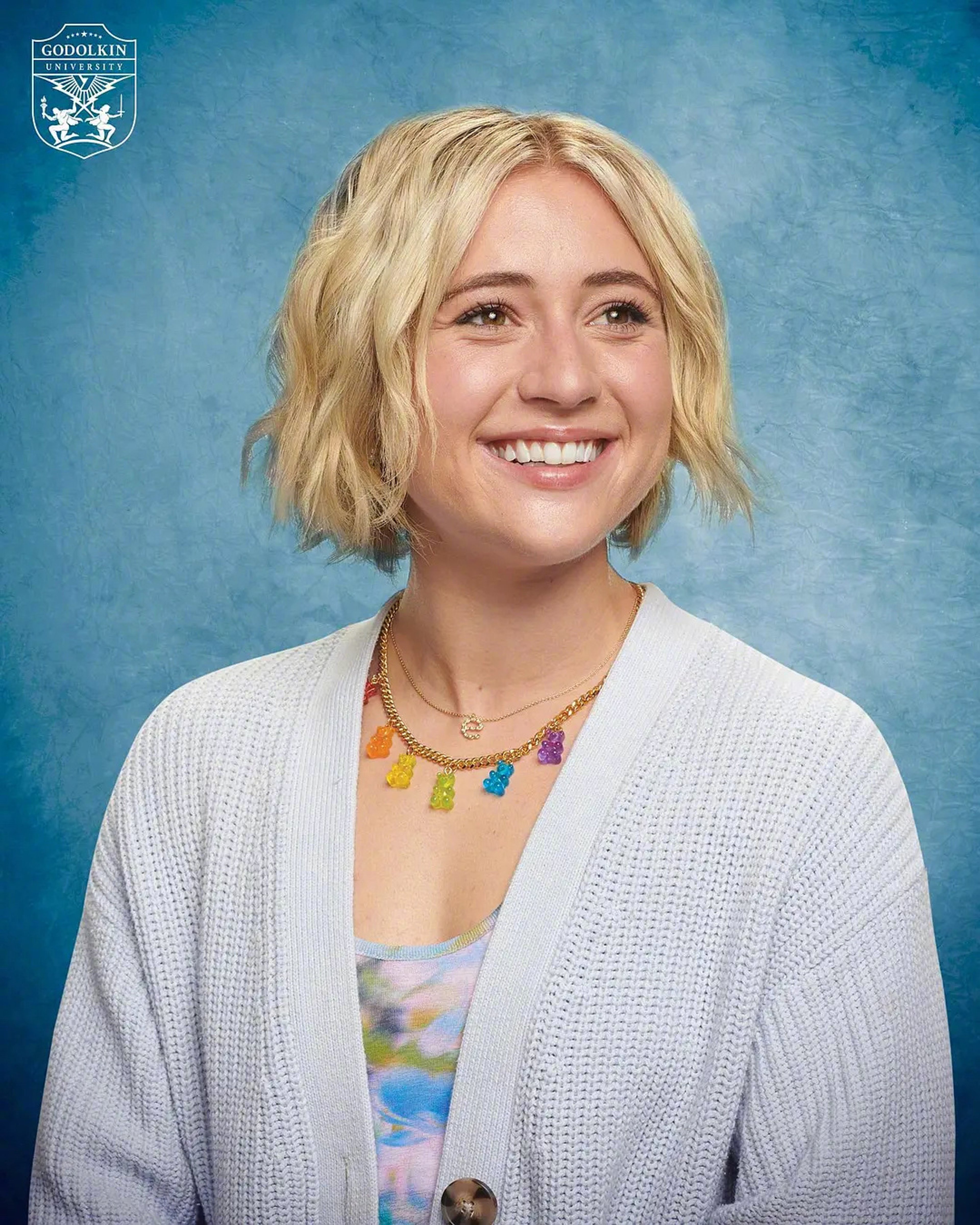 A young blonde woman with a friendly smile, wearing a white cardigan against a blue background.