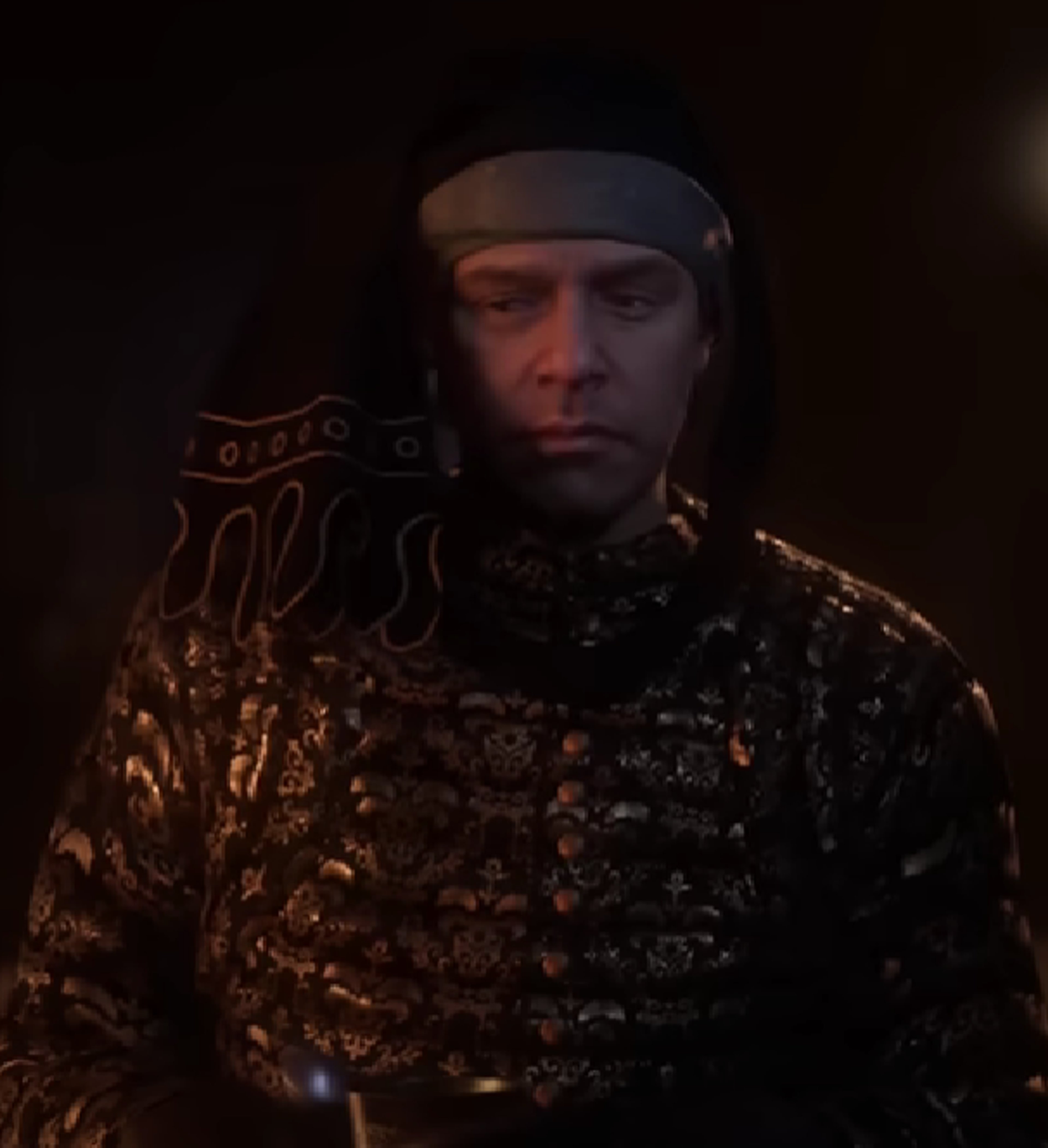 A man in a gold and black patterned robe or cloak with a serious expression