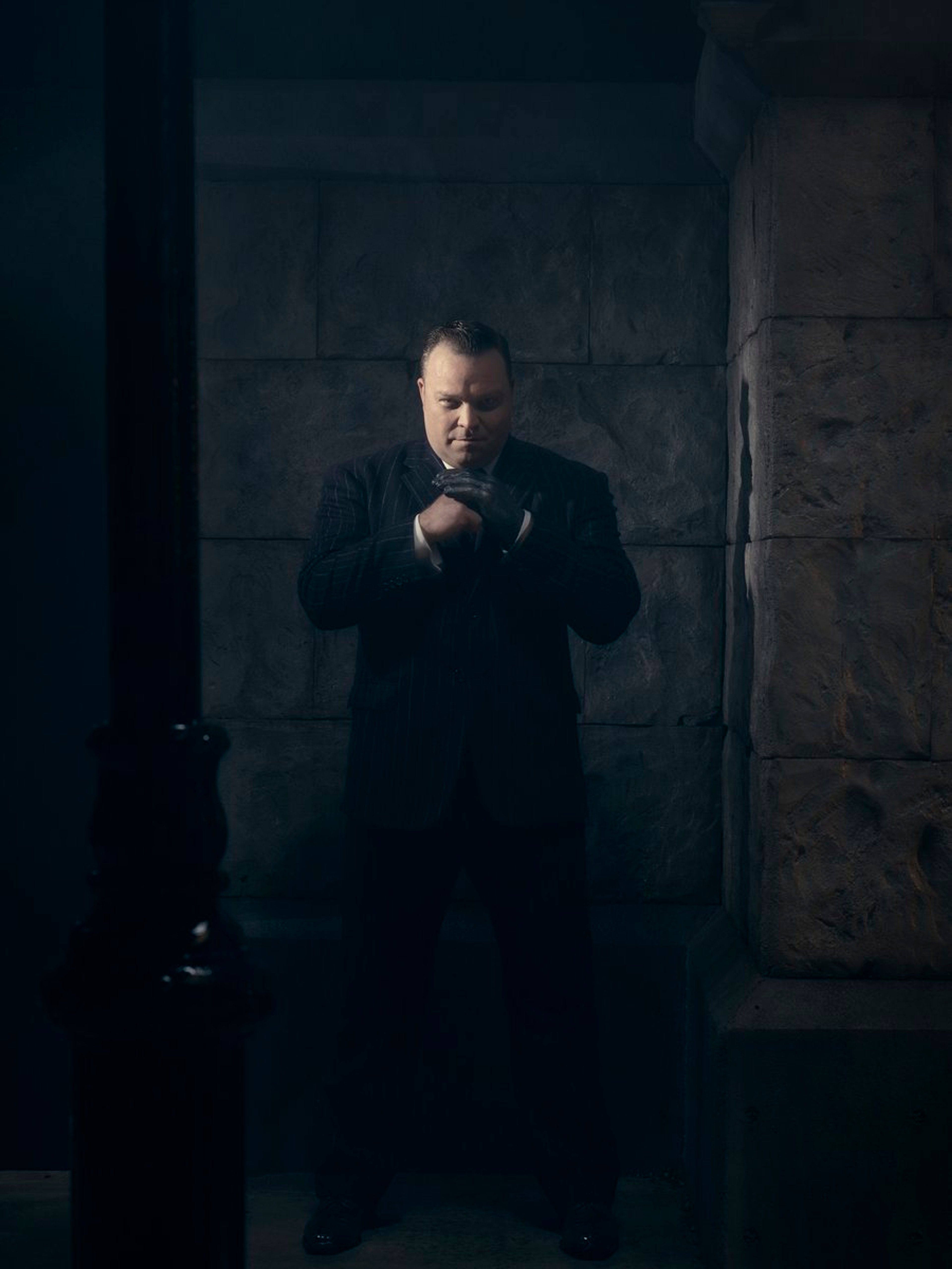 A bald, intense-looking man in a dark suit in a dimly lit industrial setting