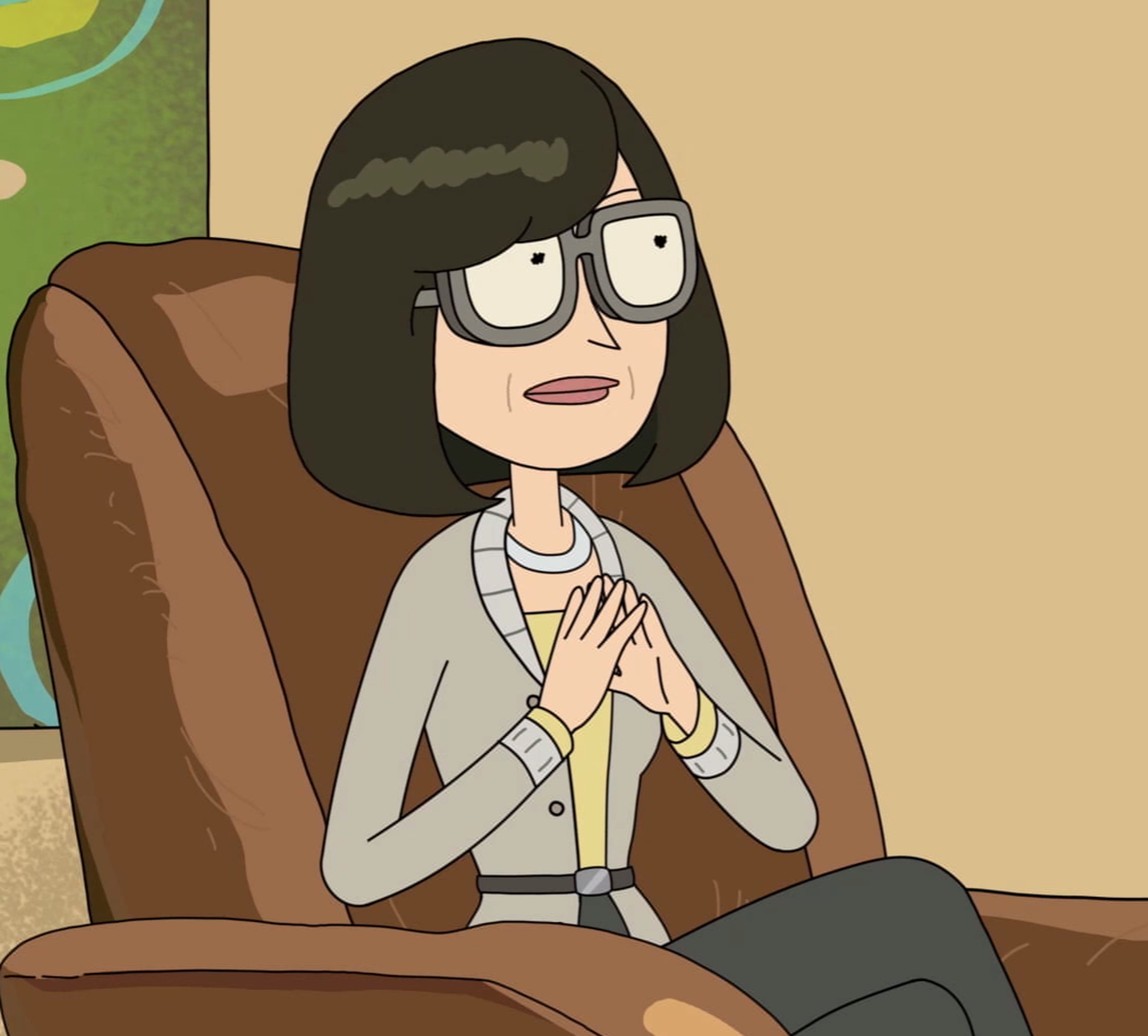 A middle-aged Asian woman with short black hair and glasses, wearing a gray sweater and sitting in a chair.