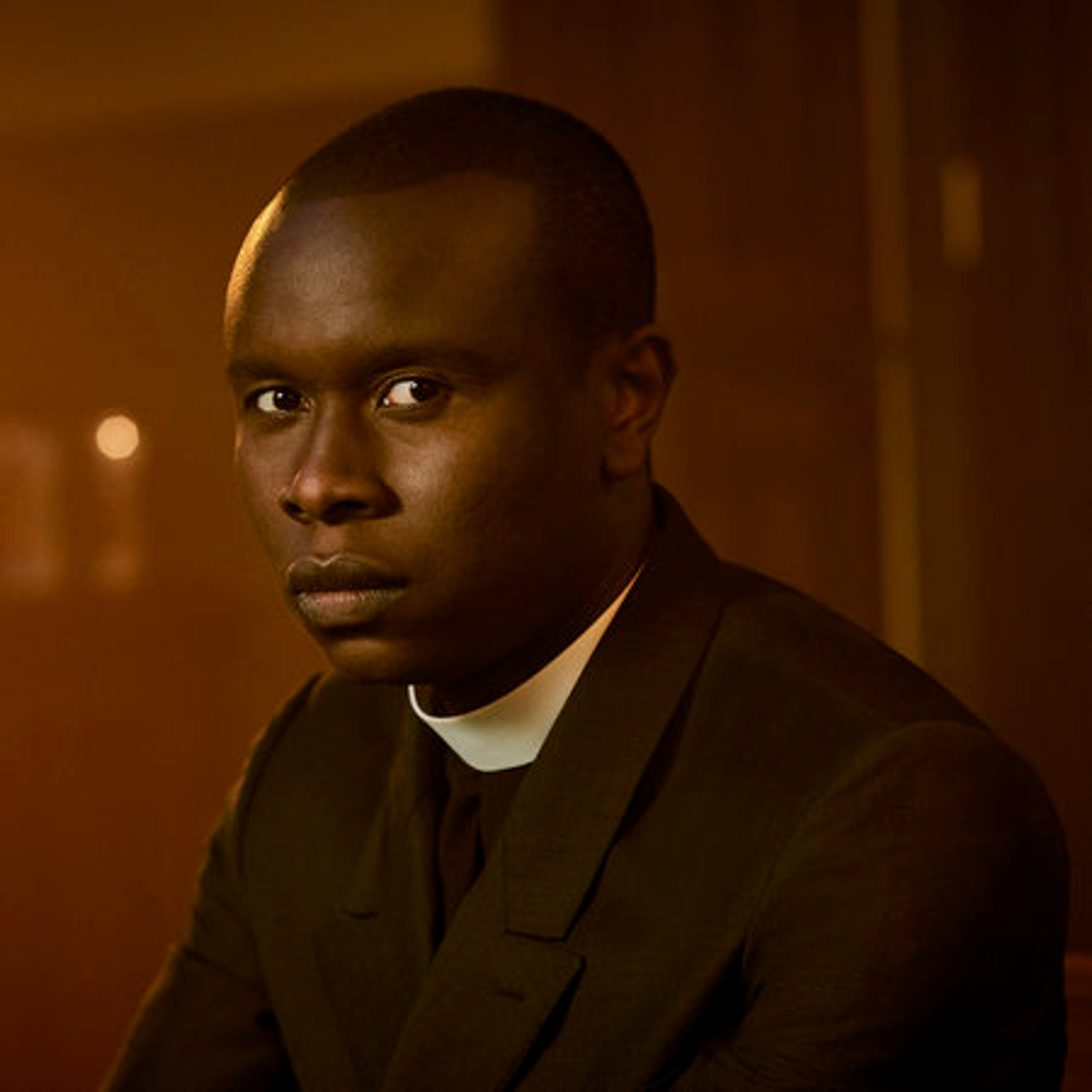 A Black man in a priest's collar with a serious expression
