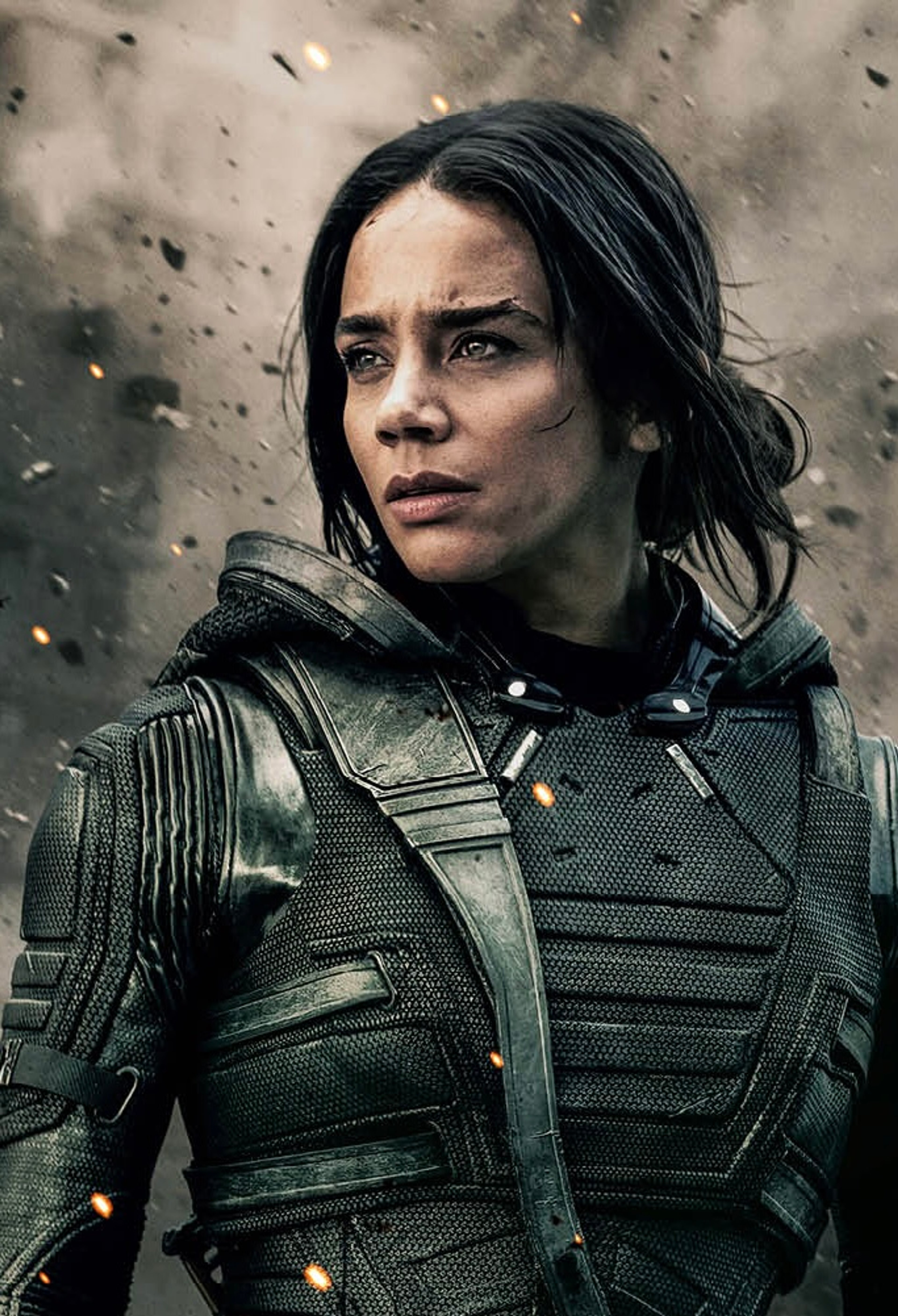A woman in a green tactical suit with a serious expression on her face in an outdoor, stormy environment.