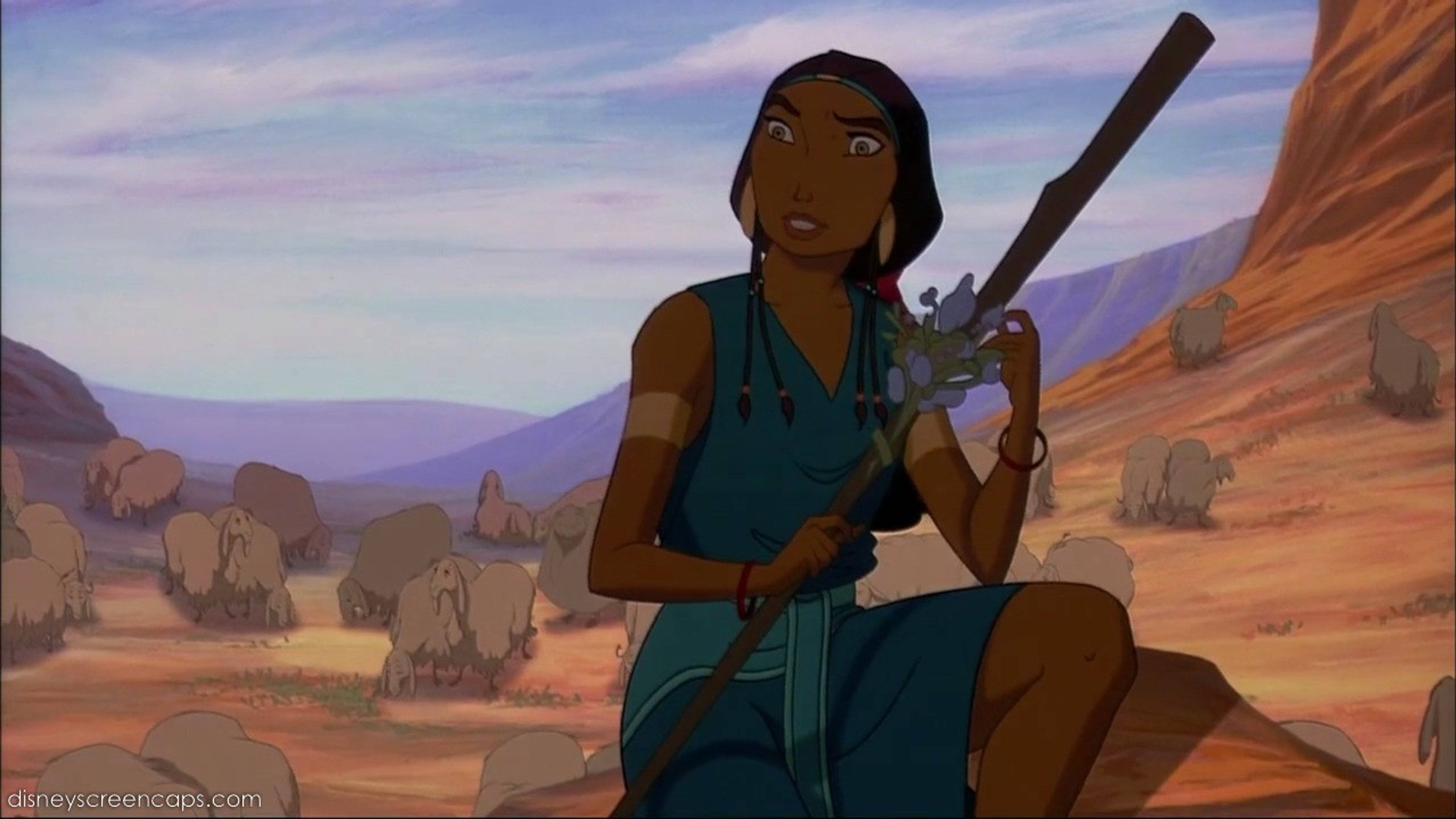 A young woman with dark skin and long hair, wearing a blue dress and holding a staff, standing in a desert landscape.