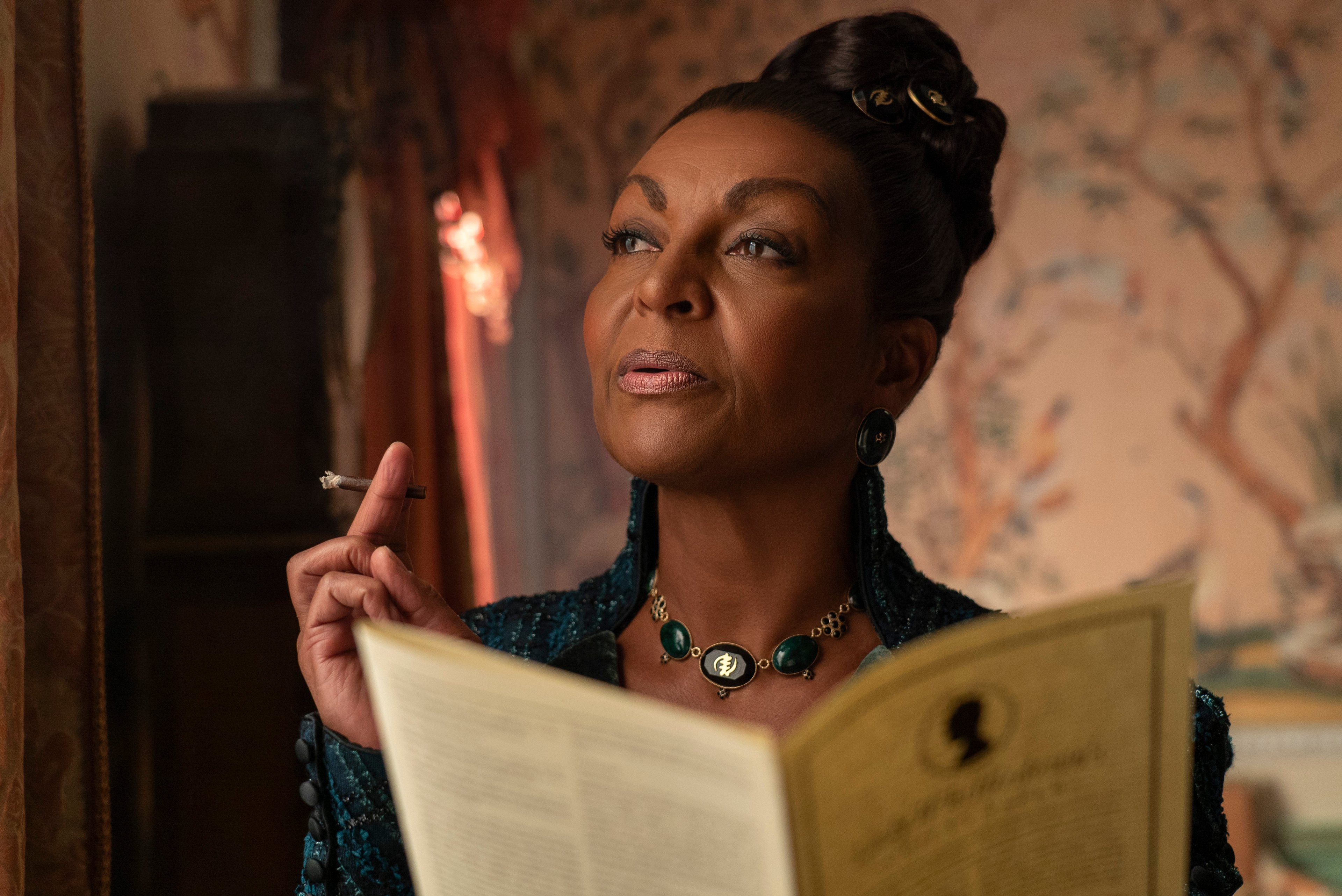 A mature, sophisticated Black woman in a dark dress holding a book