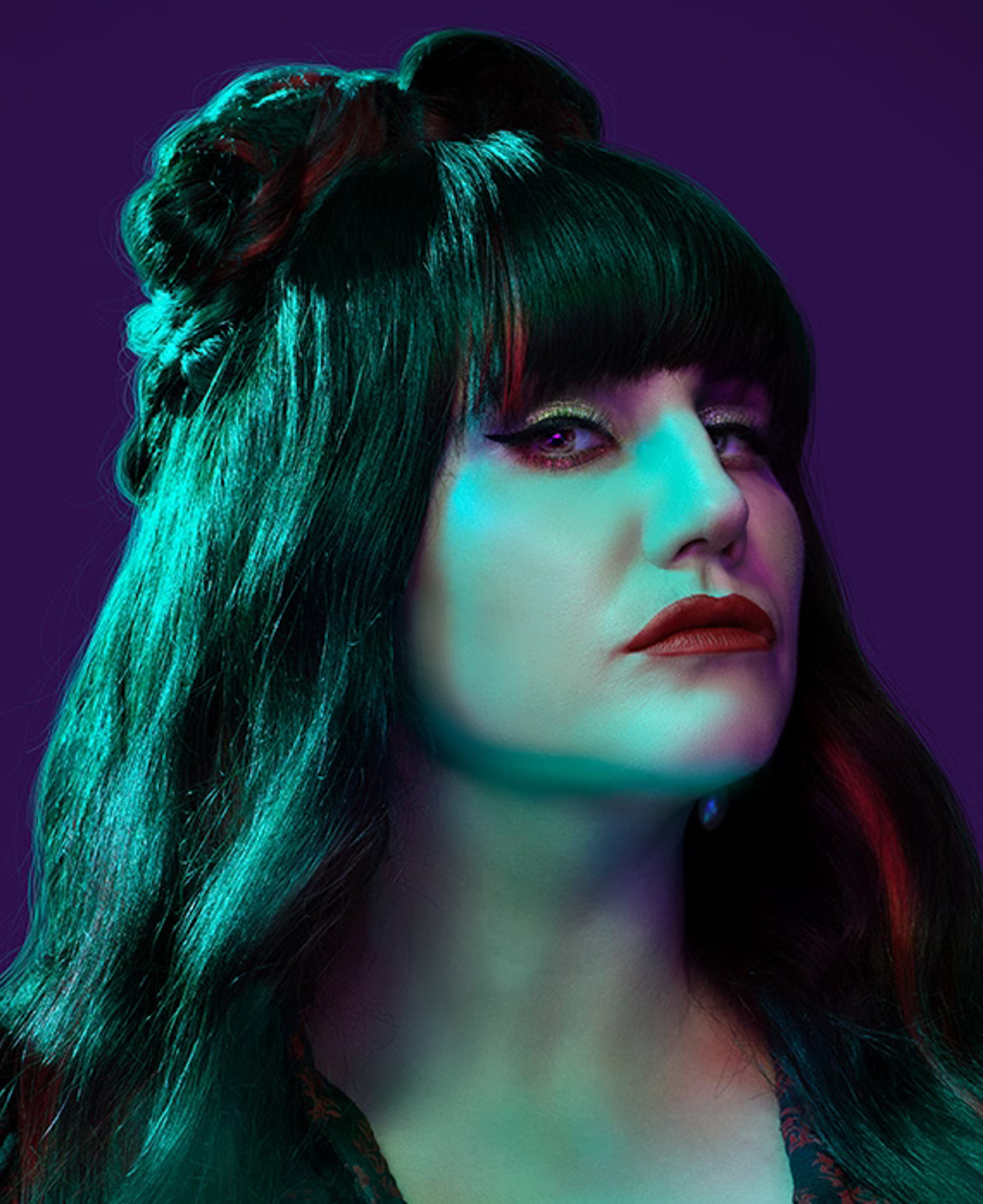 A woman with dark green hair and pale skin, wearing a high-collared dark outfit, against a purple and teal background.