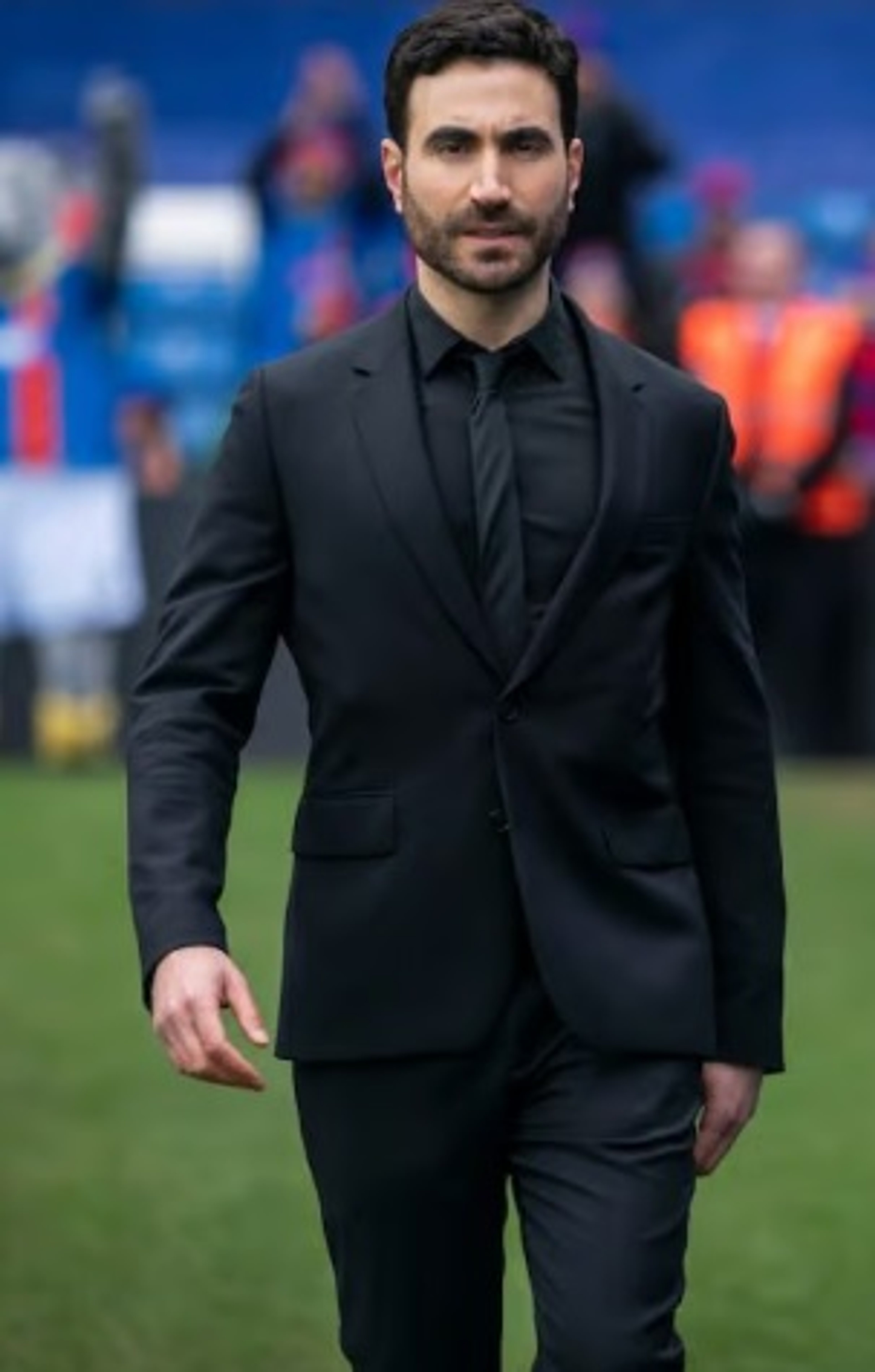 A man in a black suit standing on a soccer field