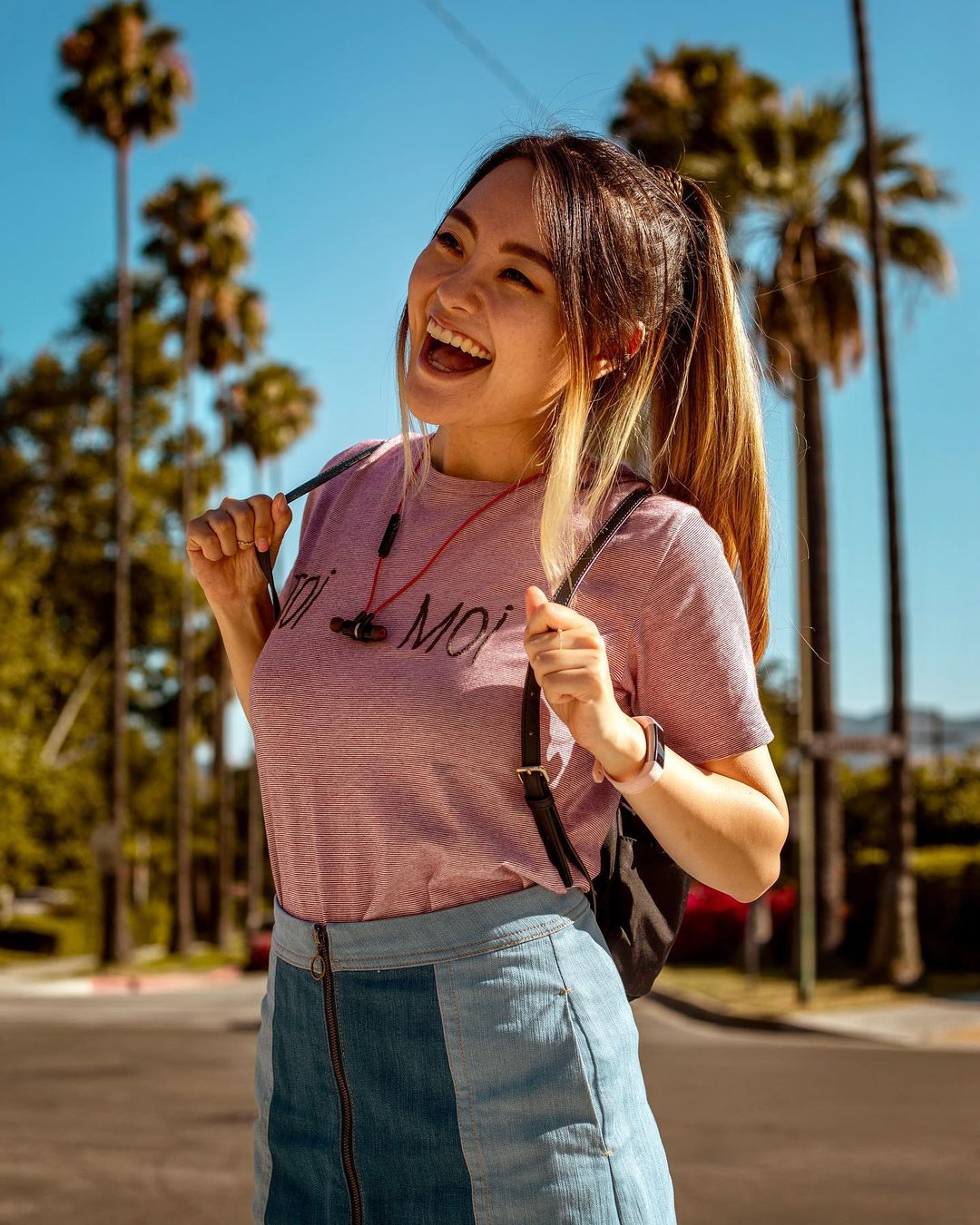 A young woman with long brown hair smiling and laughing outdoors