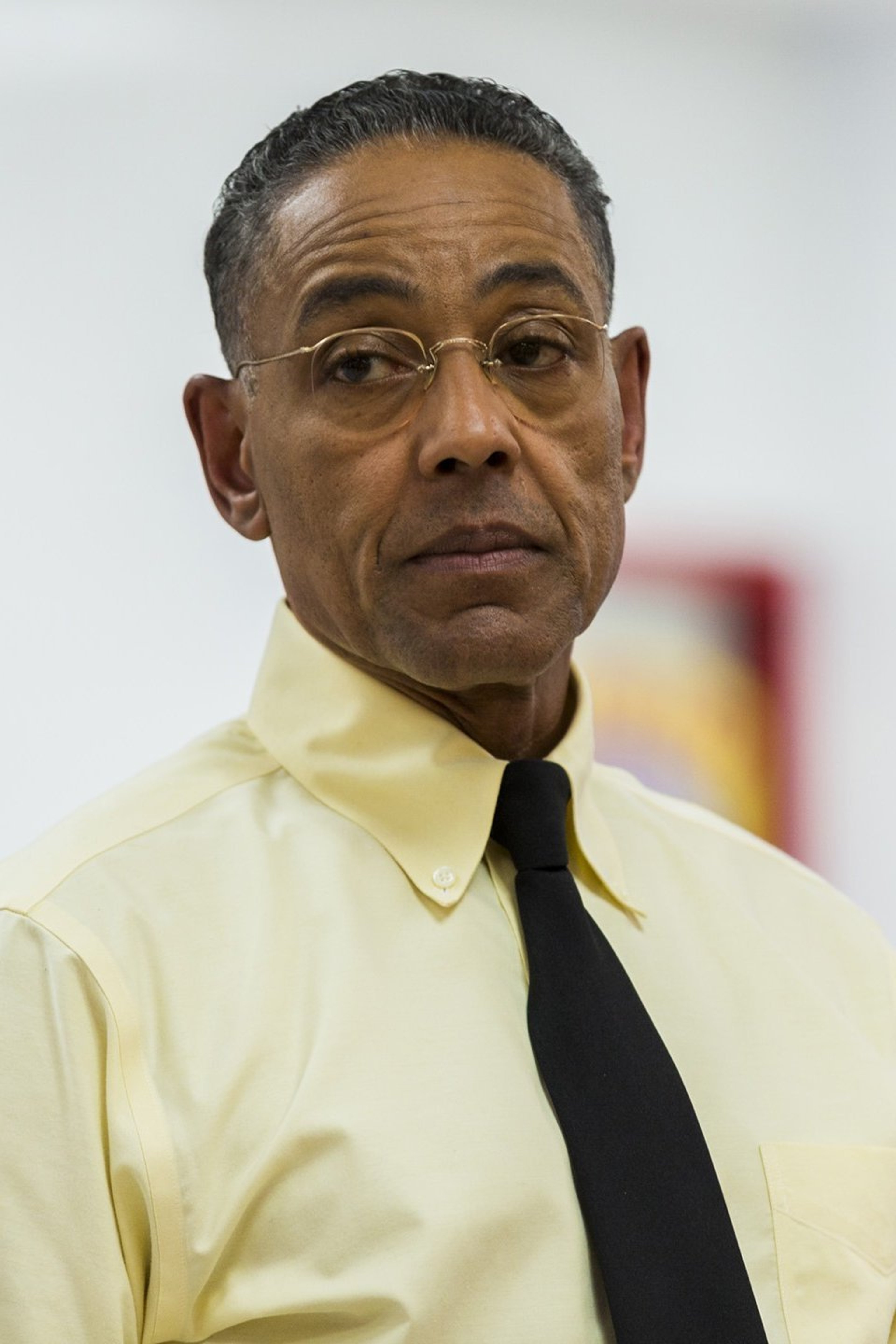 A middle-aged man with a serious expression wearing a light yellow shirt and black tie