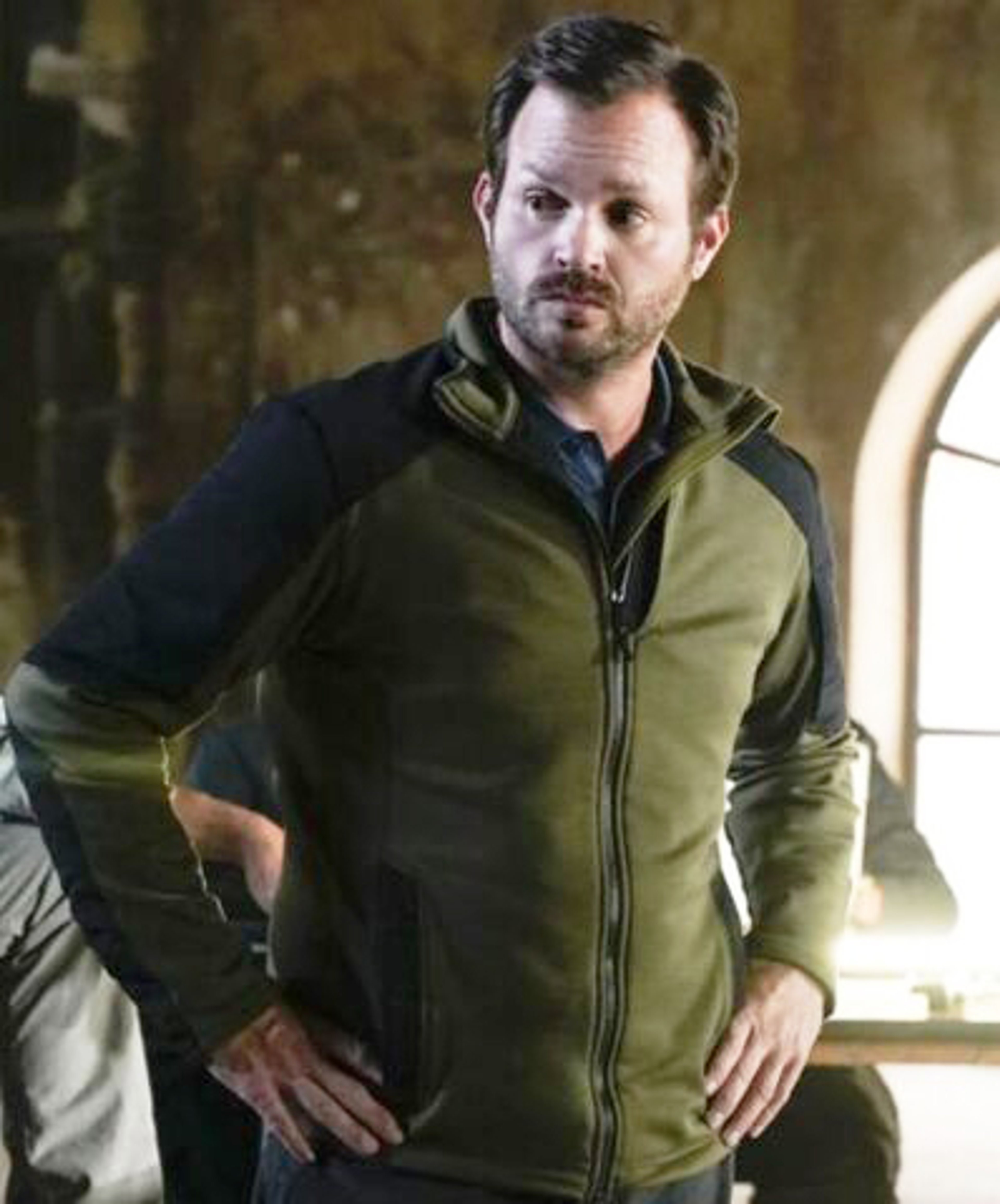 A middle-aged man in a military-style jacket standing with his hands in his pockets