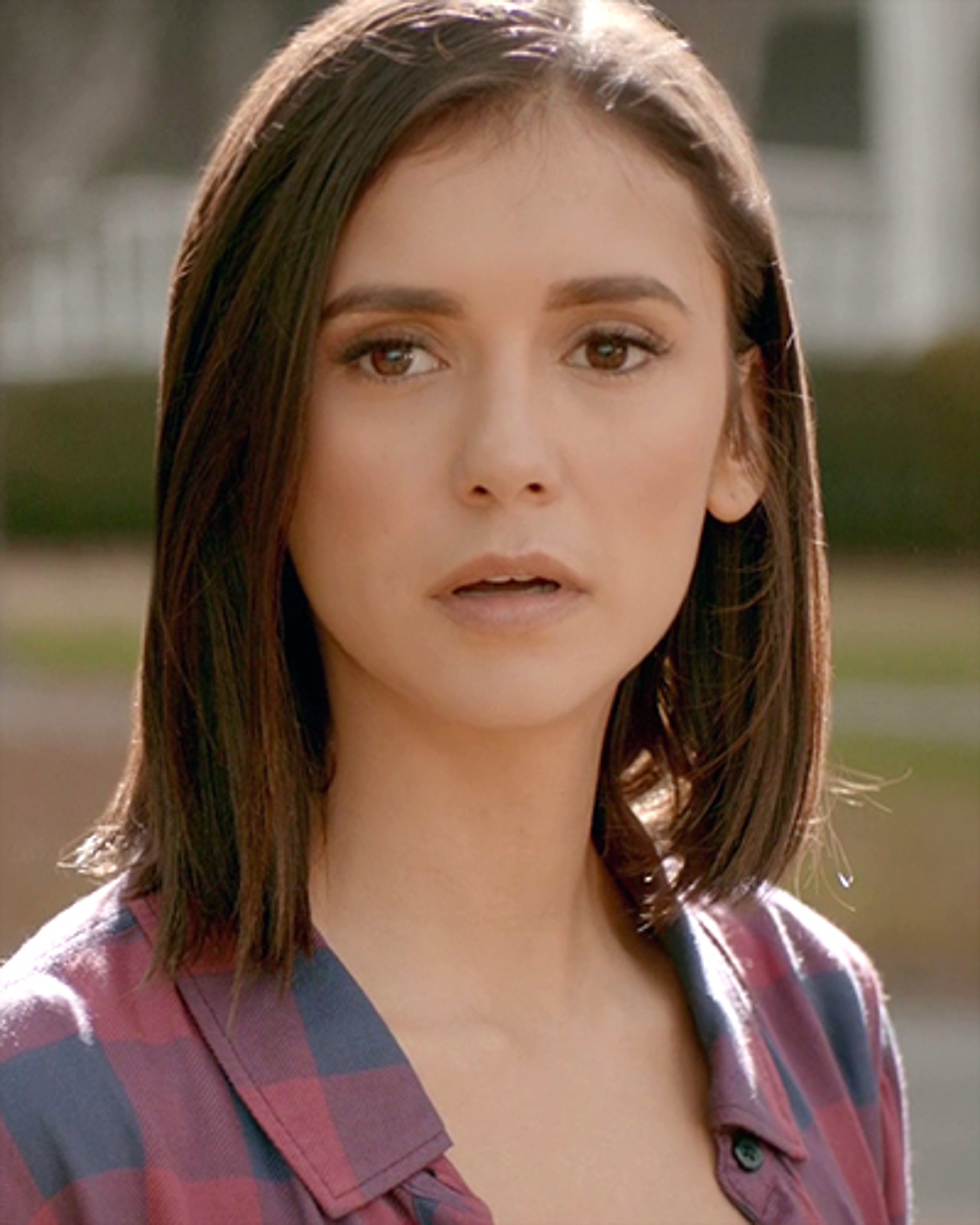 A young woman with long brown hair wearing a pink and blue plaid shirt