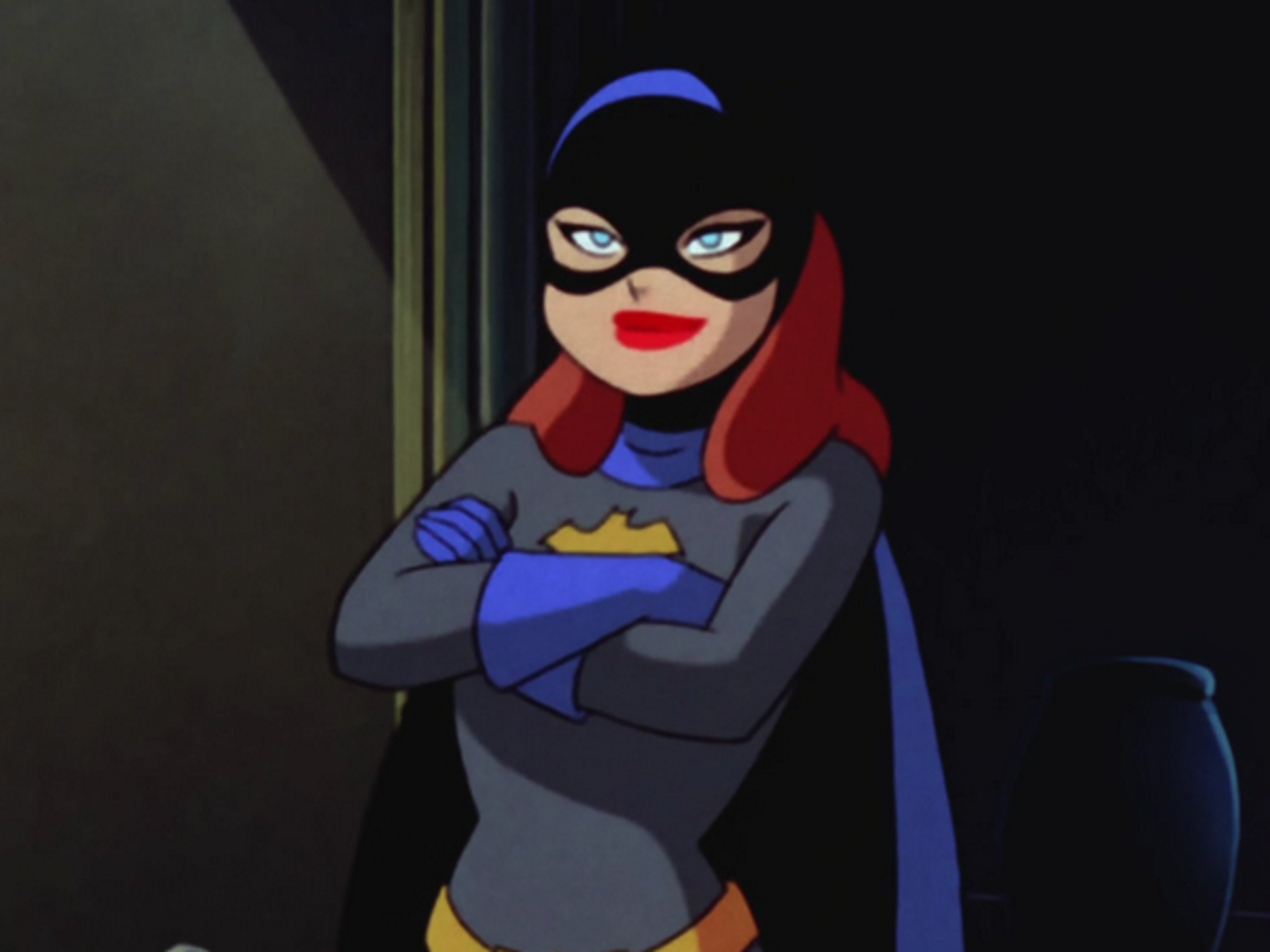 A female superhero character in a blue and black costume with a bat symbol, standing with her arms crossed